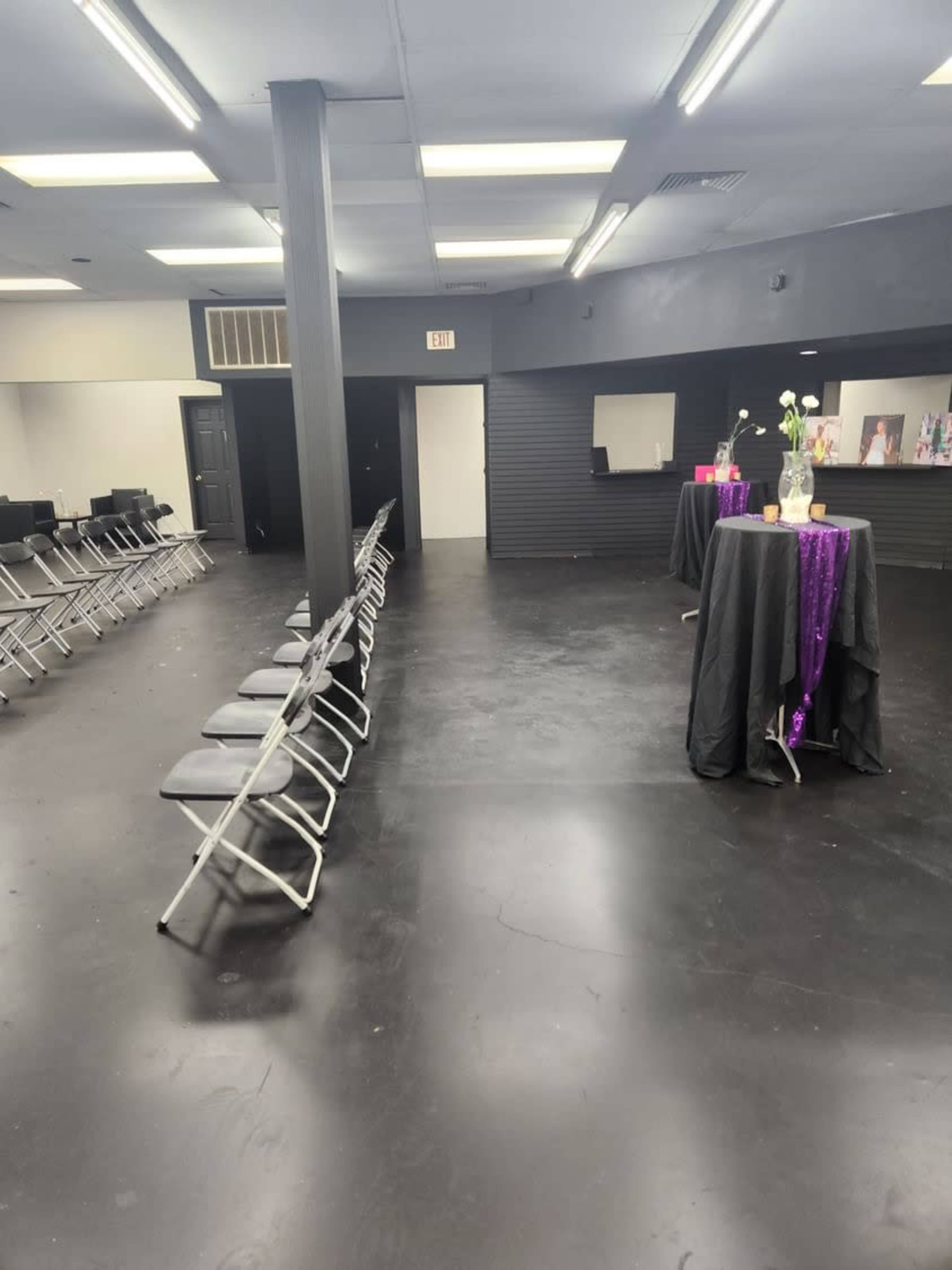 A spacious, empty room with rows of folding chairs on one side and a table covered with a black cloth and a purple sequined tablecloth on the other.