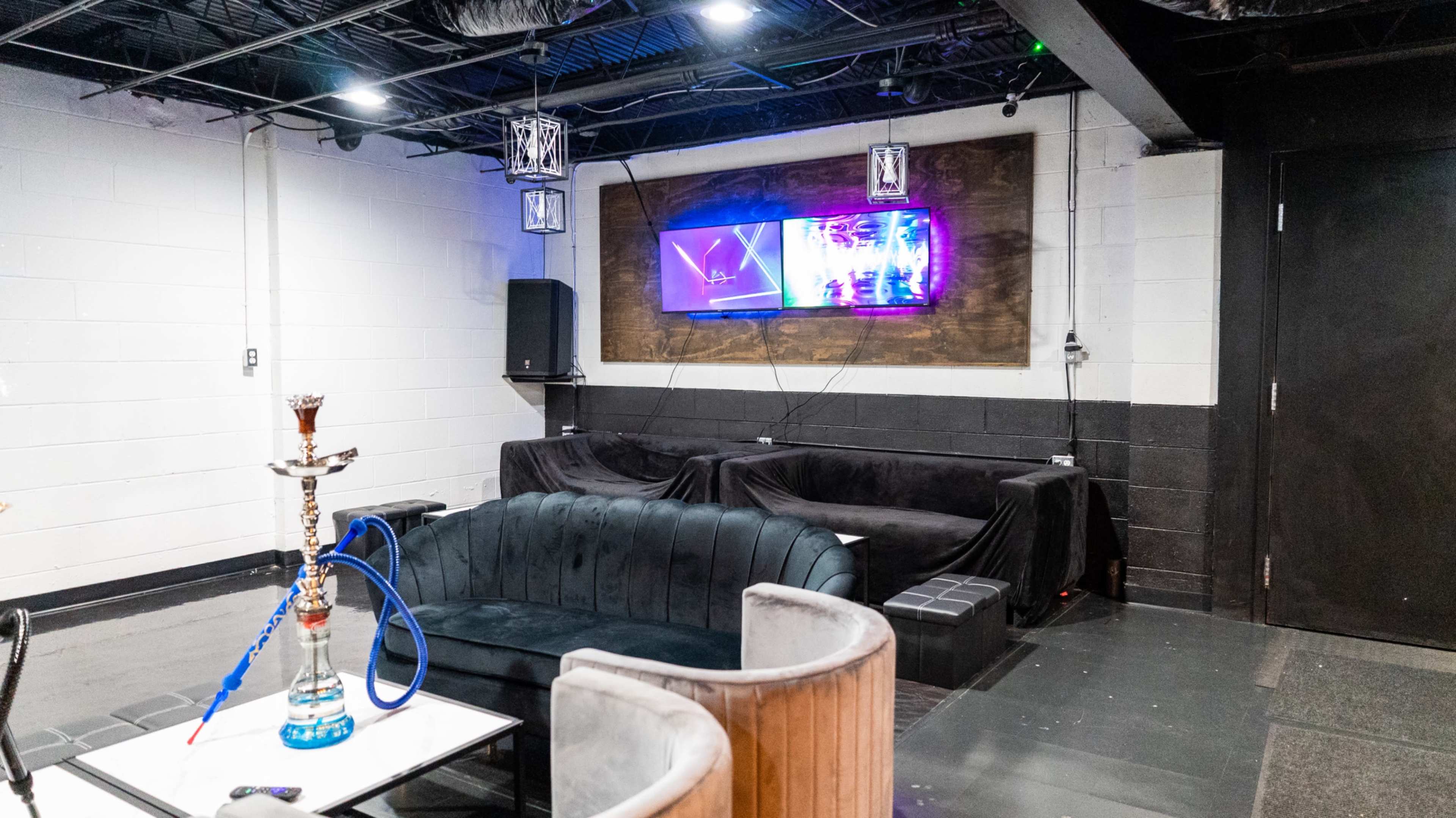 A lounge area features a hookah, a wall-mounted television, and several sofas arranged against the walls.
