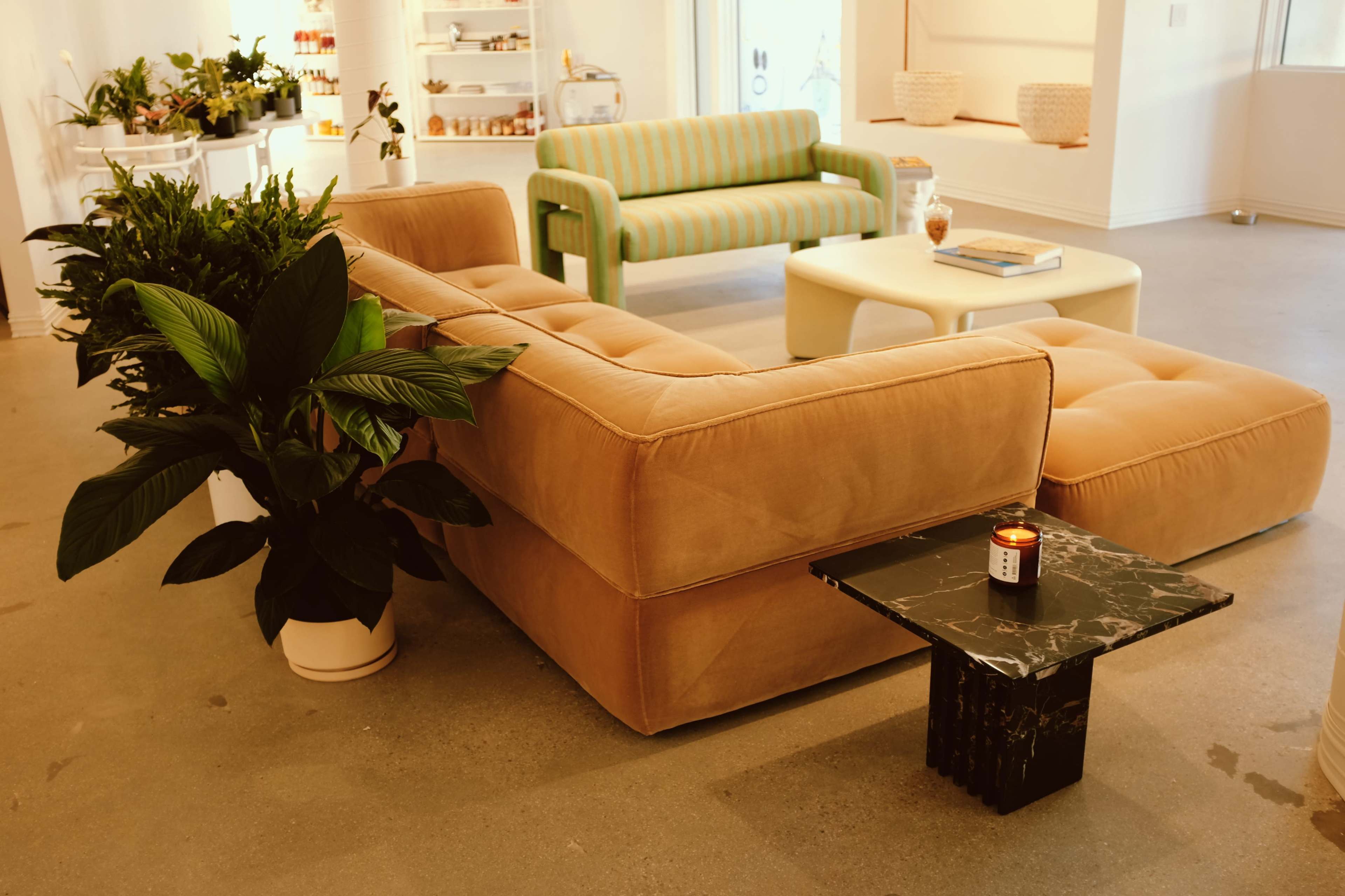 A stylish living room featuring a large, tan sectional sofa, a green and white striped two-seater, and a black marble side table with a candle.