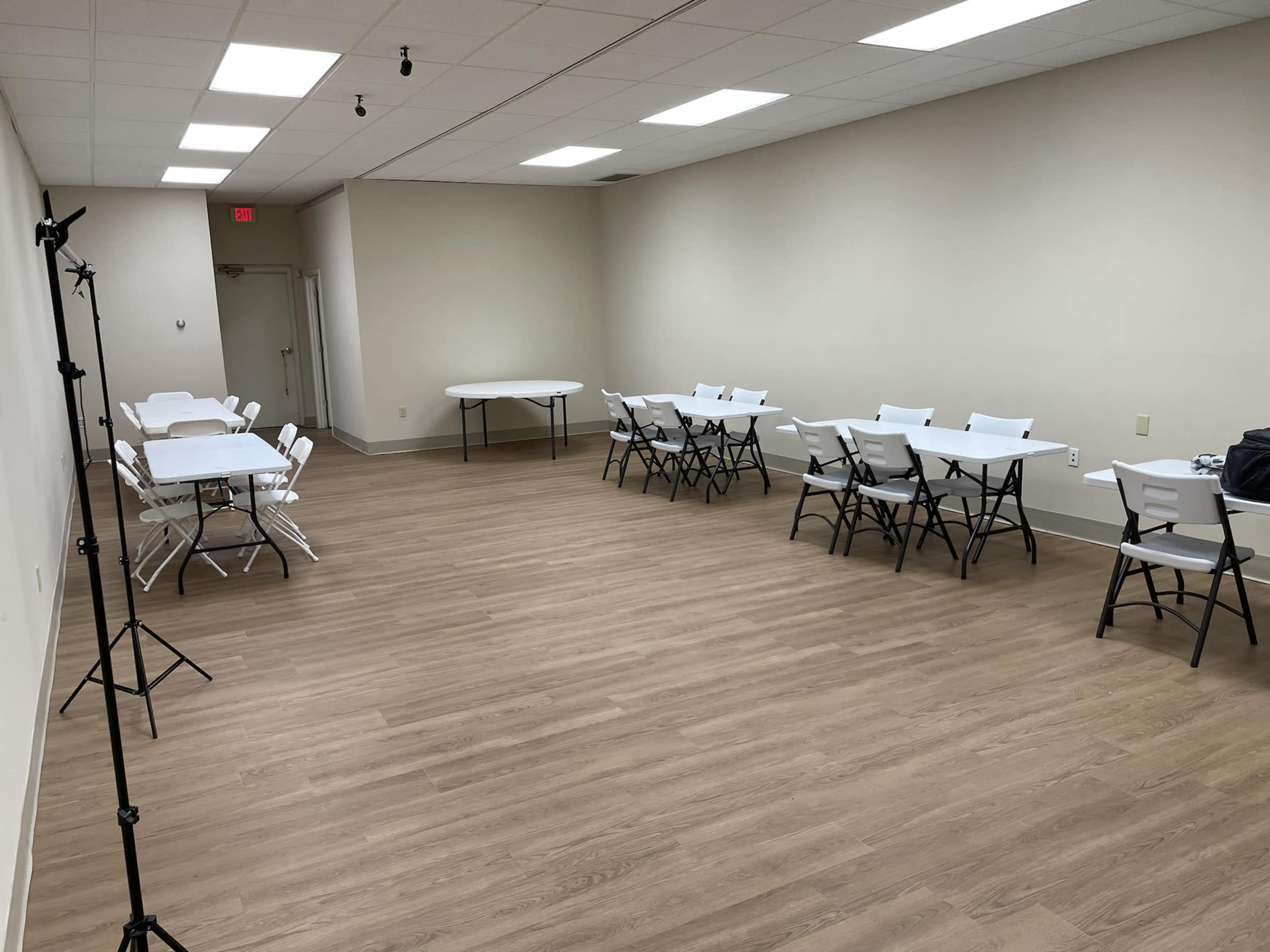 A spacious, empty room with several tables and chairs arranged methodically on a wooden floor.