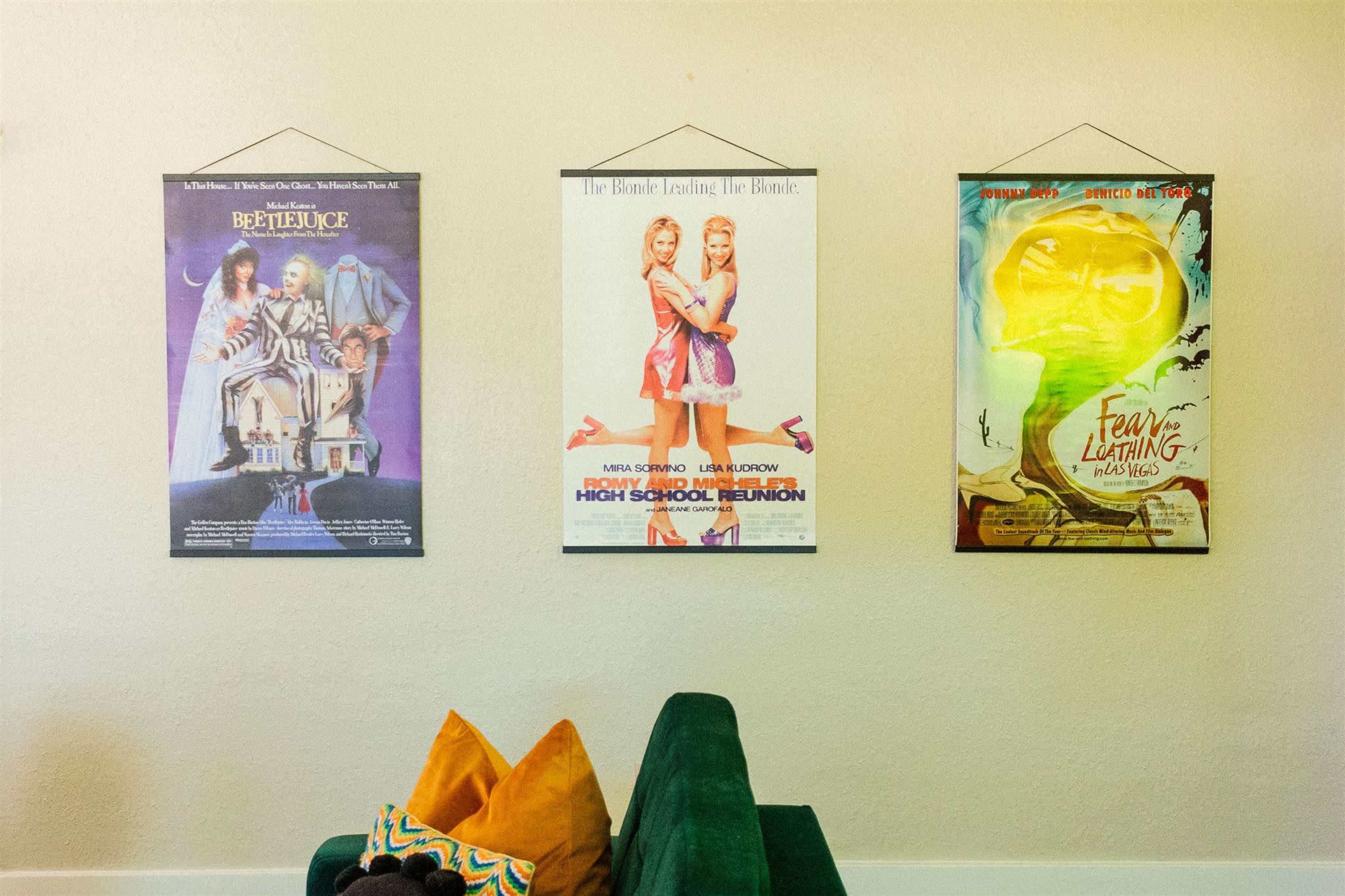 Three movie posters hang on the wall above a green sofa, featuring "Beetlejuice," "High School Reunion," and "Fear and Loathing in Las Vegas."