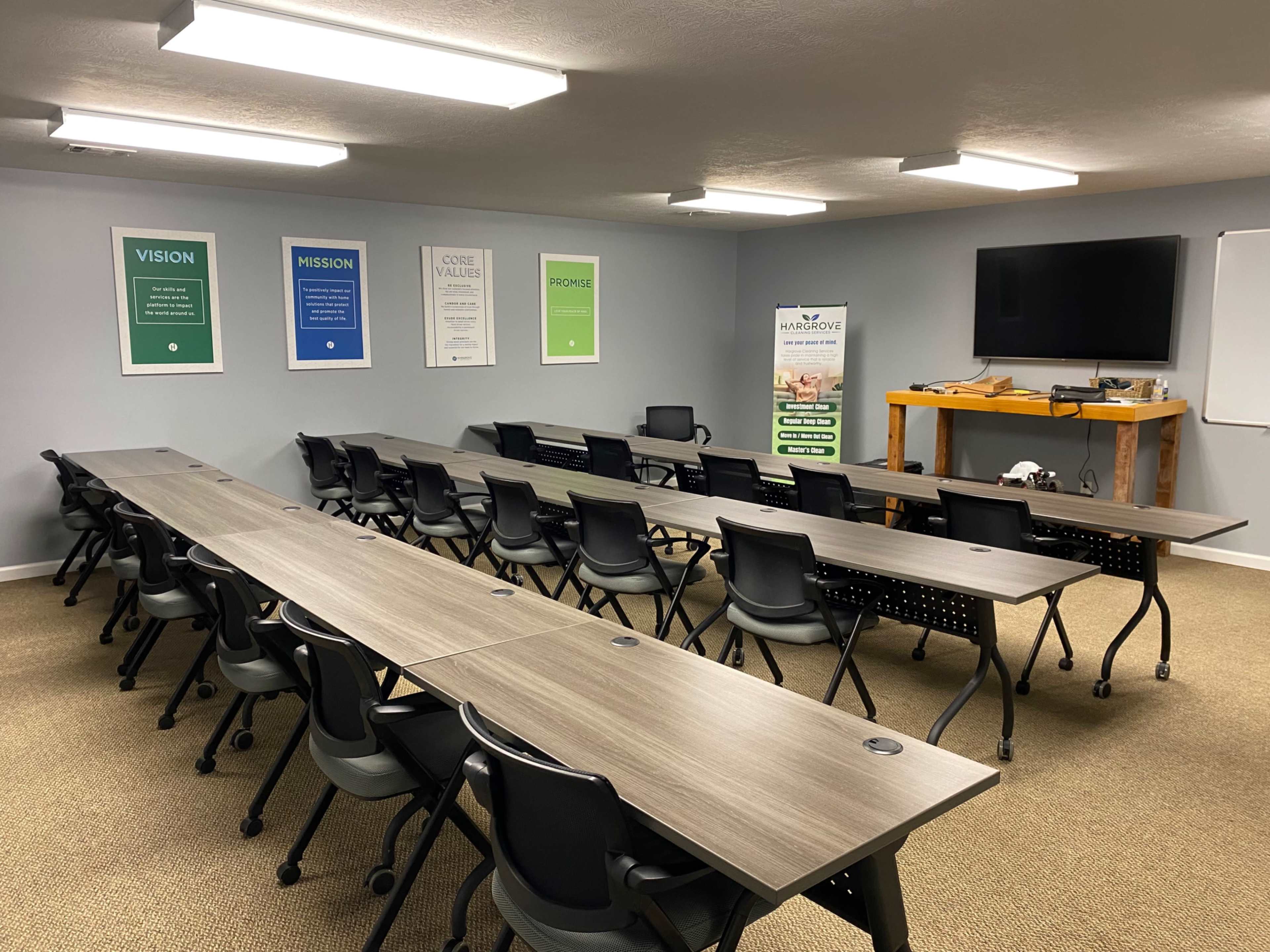 A conference room with several rows of tables and chairs arranged for meetings, along with posters on the walls and a large screen at one end.