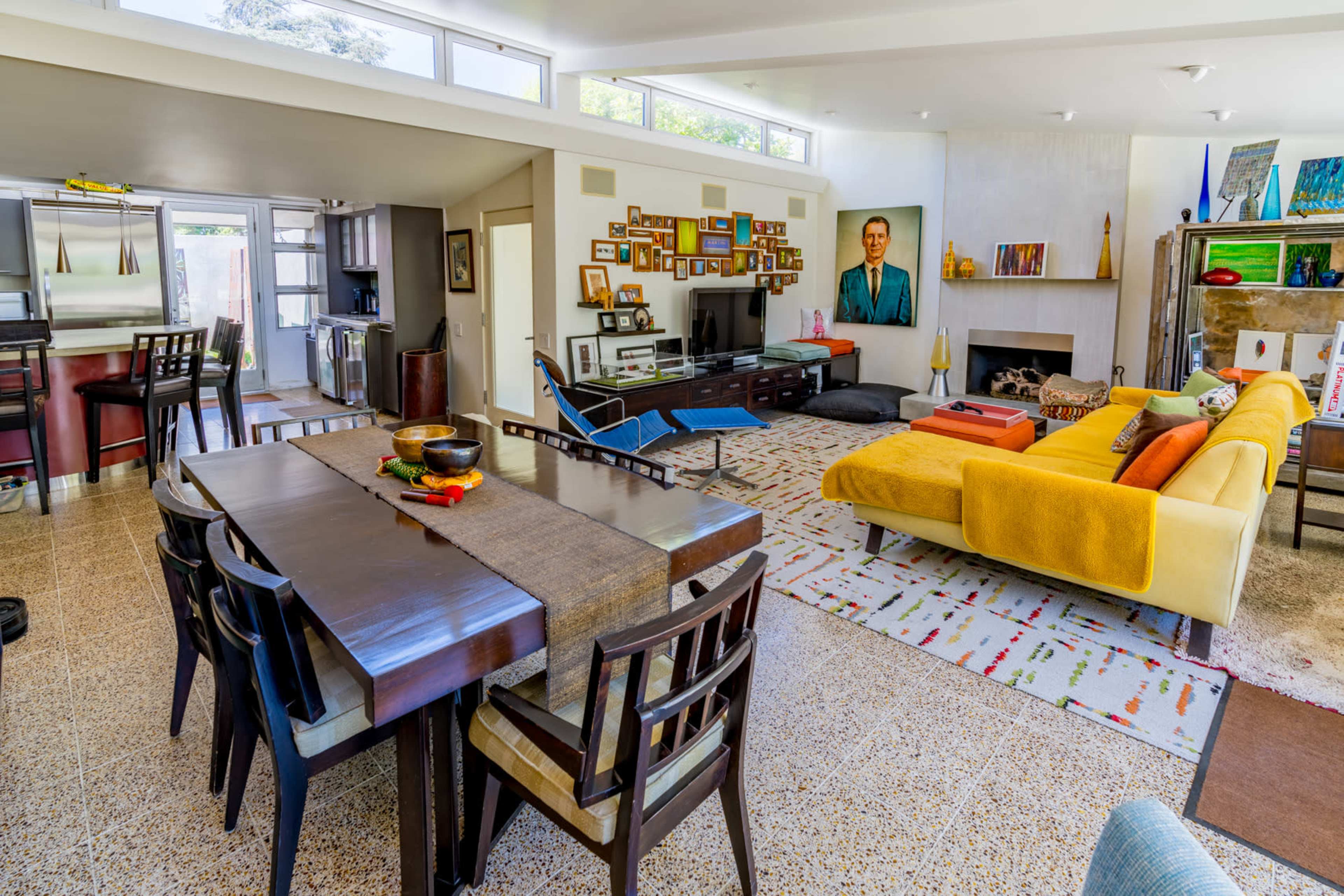 A spacious living area with a dining table, a yellow sofa, and various artworks on the walls.
