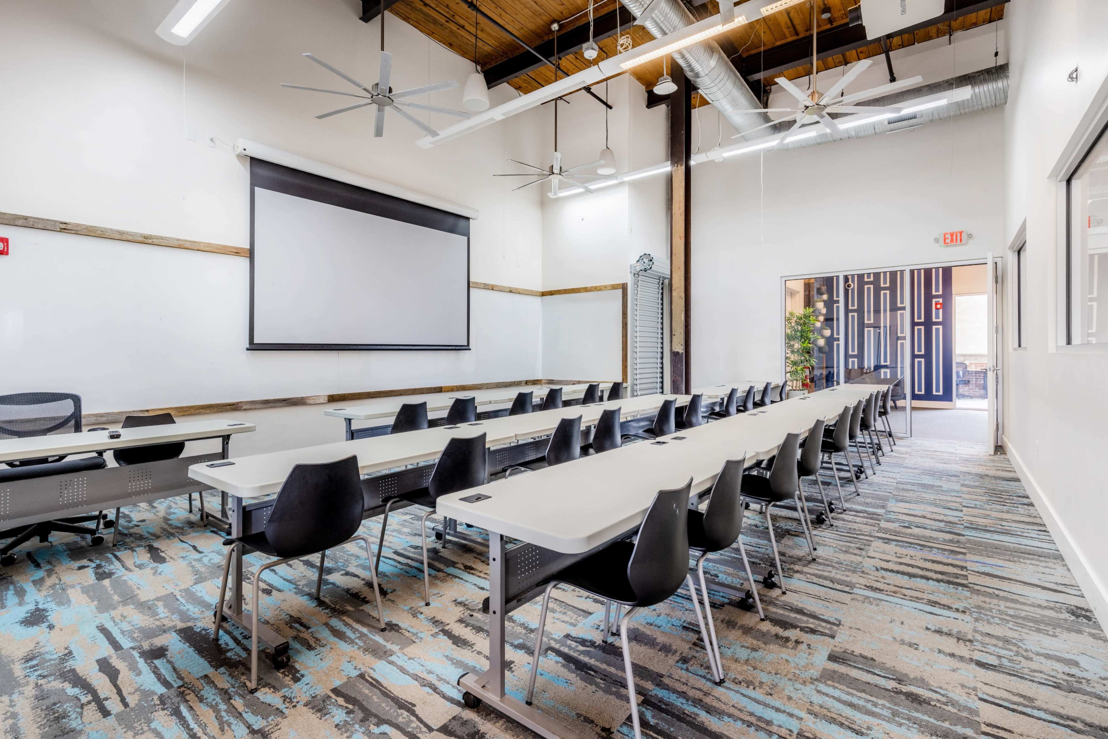 A modern classroom features rows of white tables and black chairs, a large screen at the front, and bright, overhead lighting.