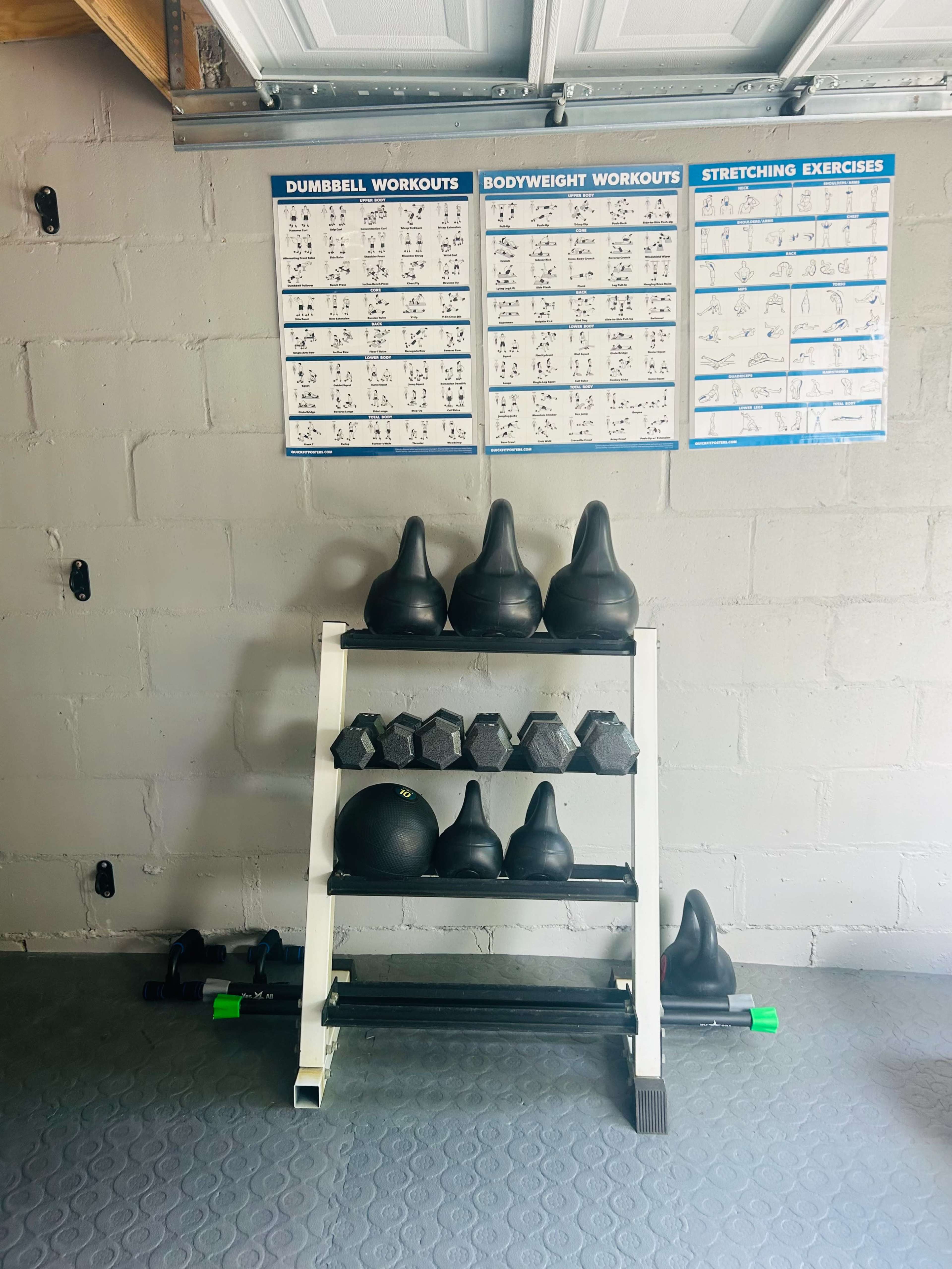A garage with a storage rack holding various weights, along with workout charts mounted on the wall above it.
