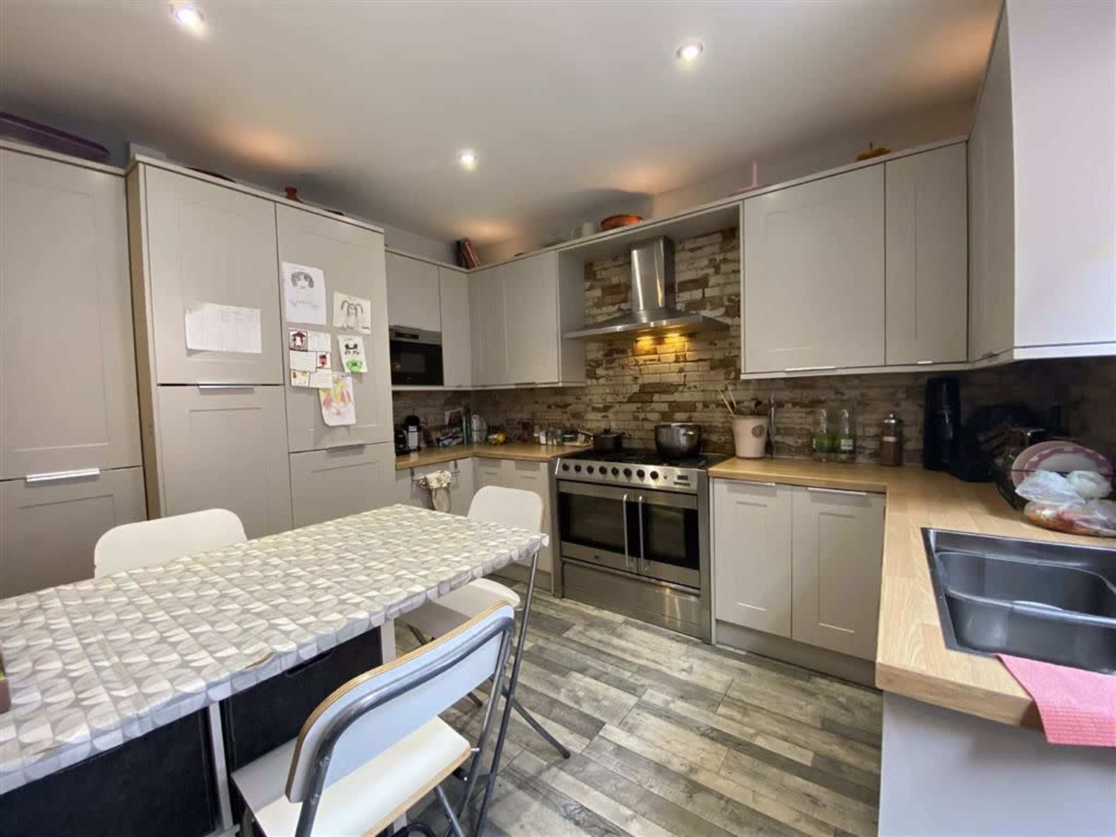 The kitchen features gray cabinetry, a tiled backsplash, a large stainless steel stove, and a table with chairs.