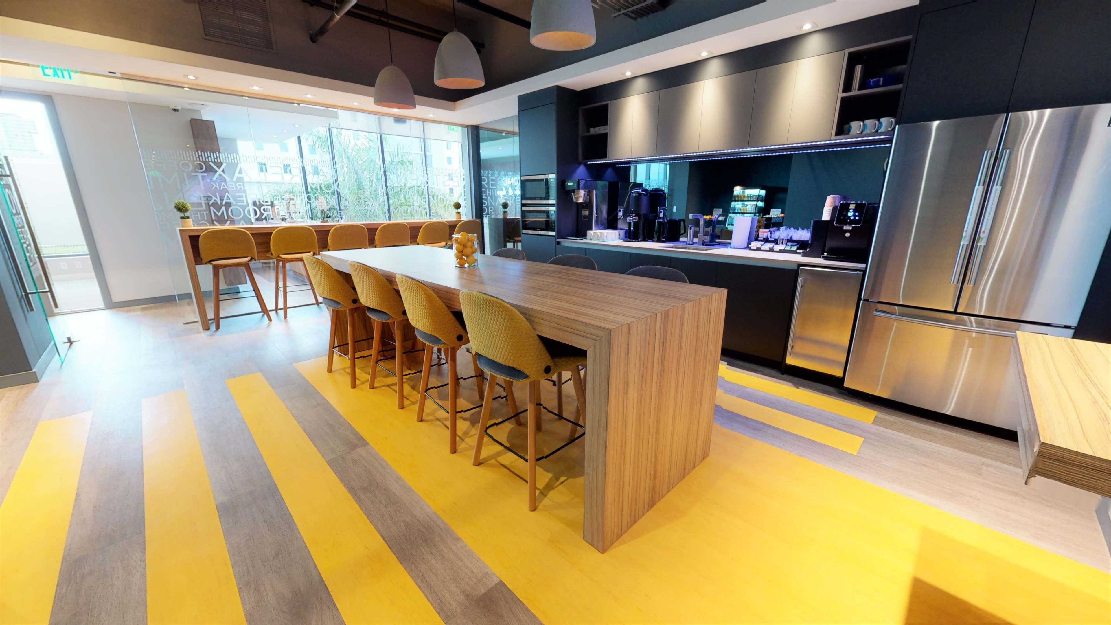 A modern kitchen area featuring a long wooden bar with high stools, a sleek countertop, and stainless steel appliances.