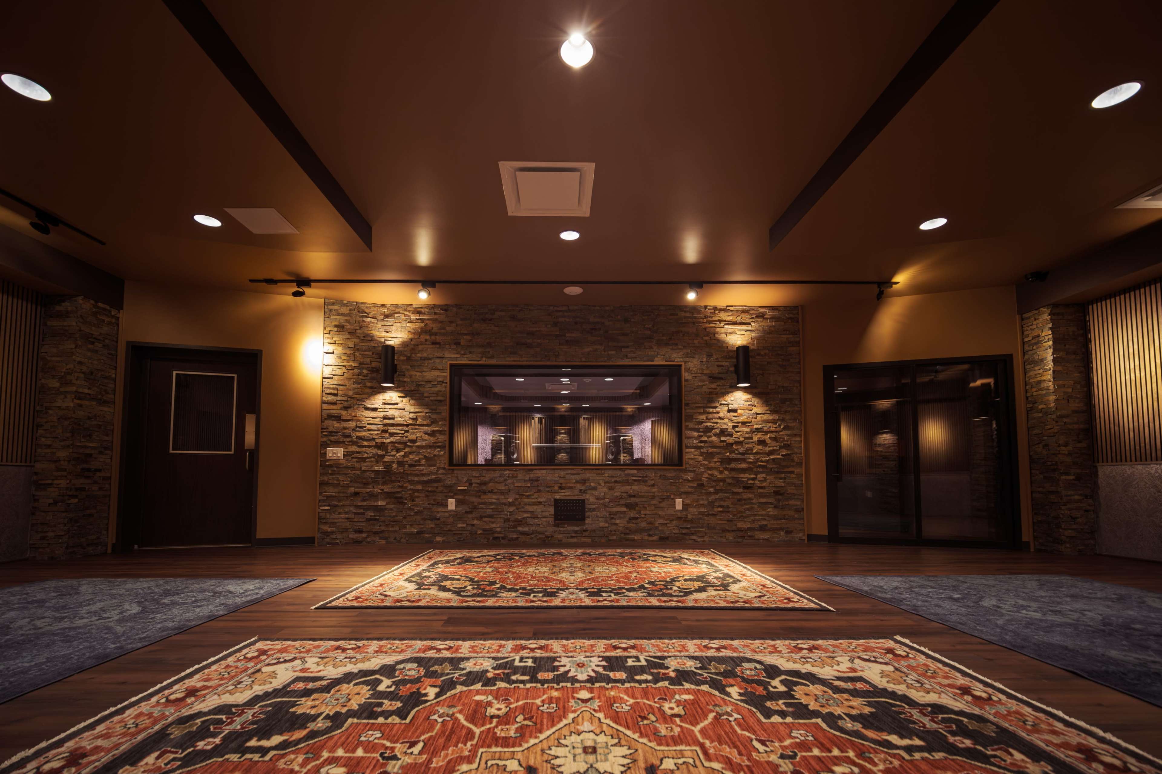 The image shows an interior room with a stone accent wall, dim lighting, and decorative rugs on a wooden floor.