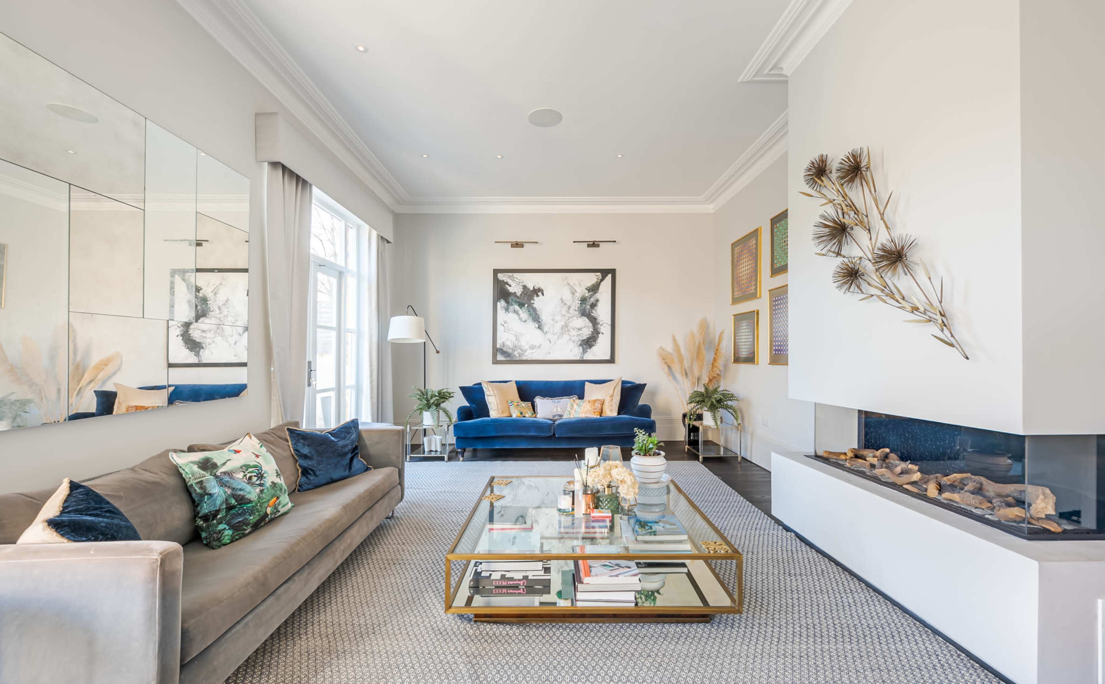 A stylish living room with a gray sofa, a blue accent chair, a coffee table with books and decorative items, and a modern fireplace.