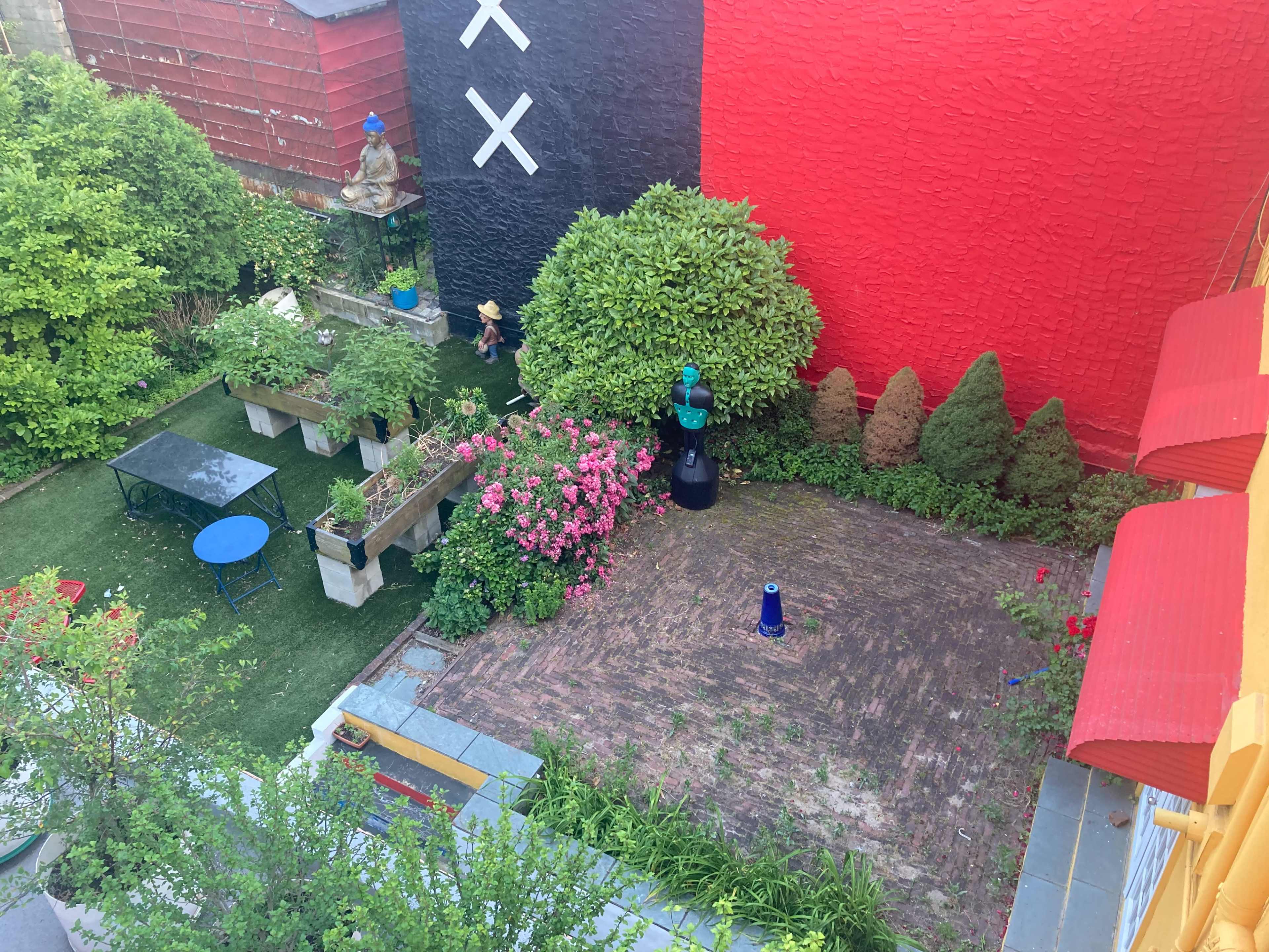 A garden area featuring a variety of plants, a stone pathway, and a small blue table surrounded by raised planters filled with flowers.