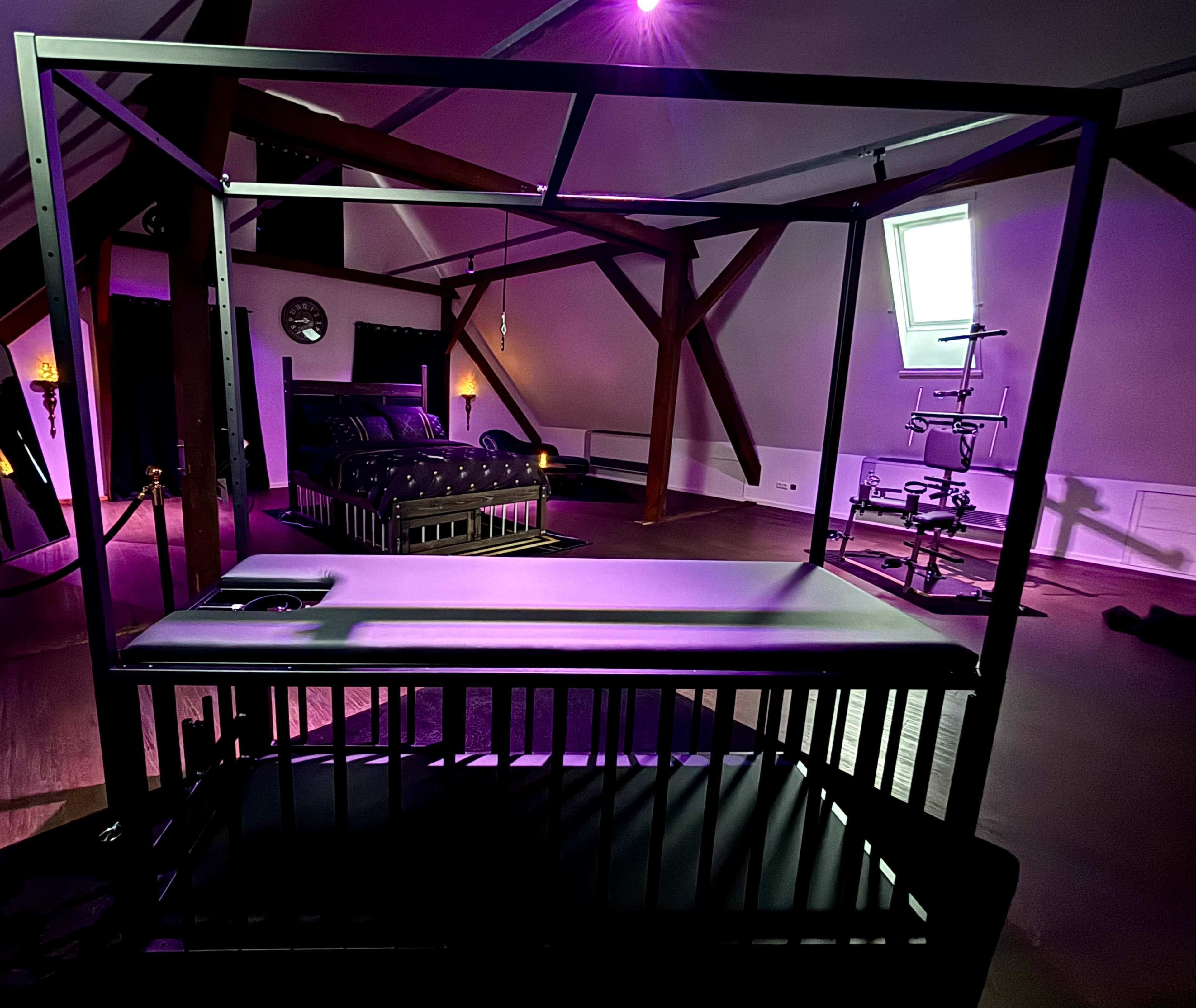 The image shows a dimly lit room with a canopy bed, adorned with purple lighting and wooden beams on the ceiling.