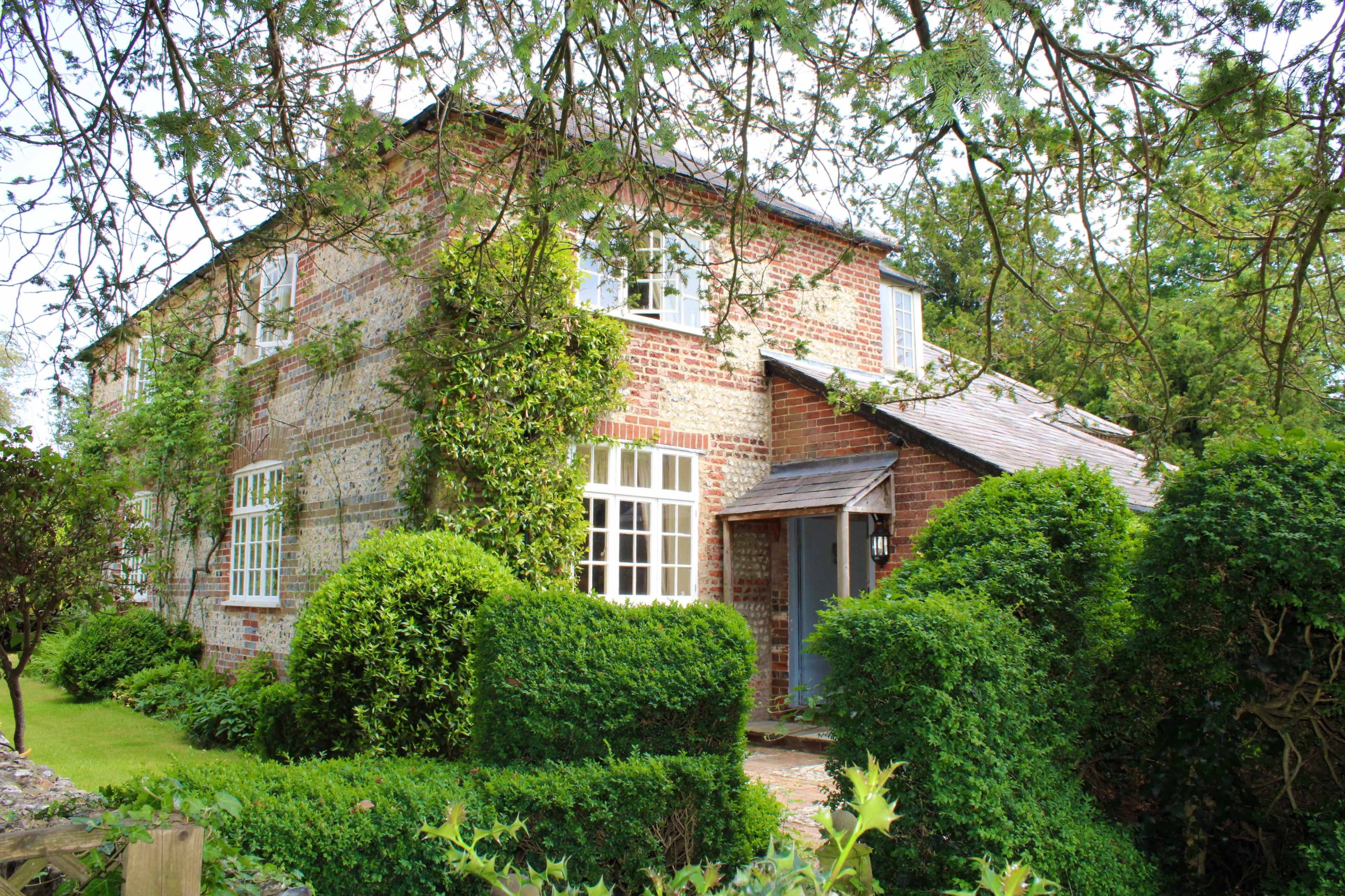 A brick house surrounded by neatly trimmed hedges and greenery.