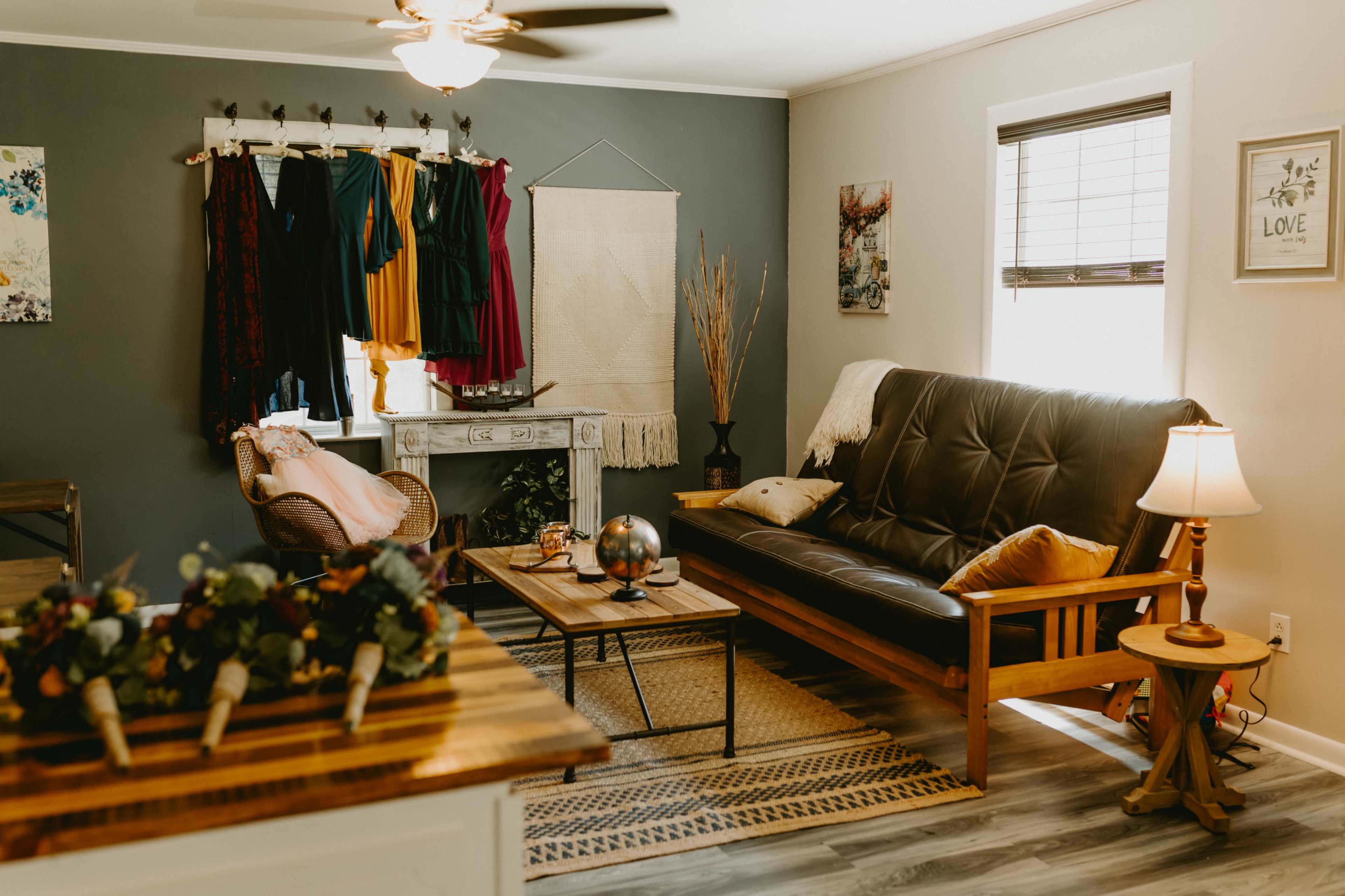 A cozy living room features a dark sofa, a wooden coffee table, and a rack of colorful dresses on the wall.