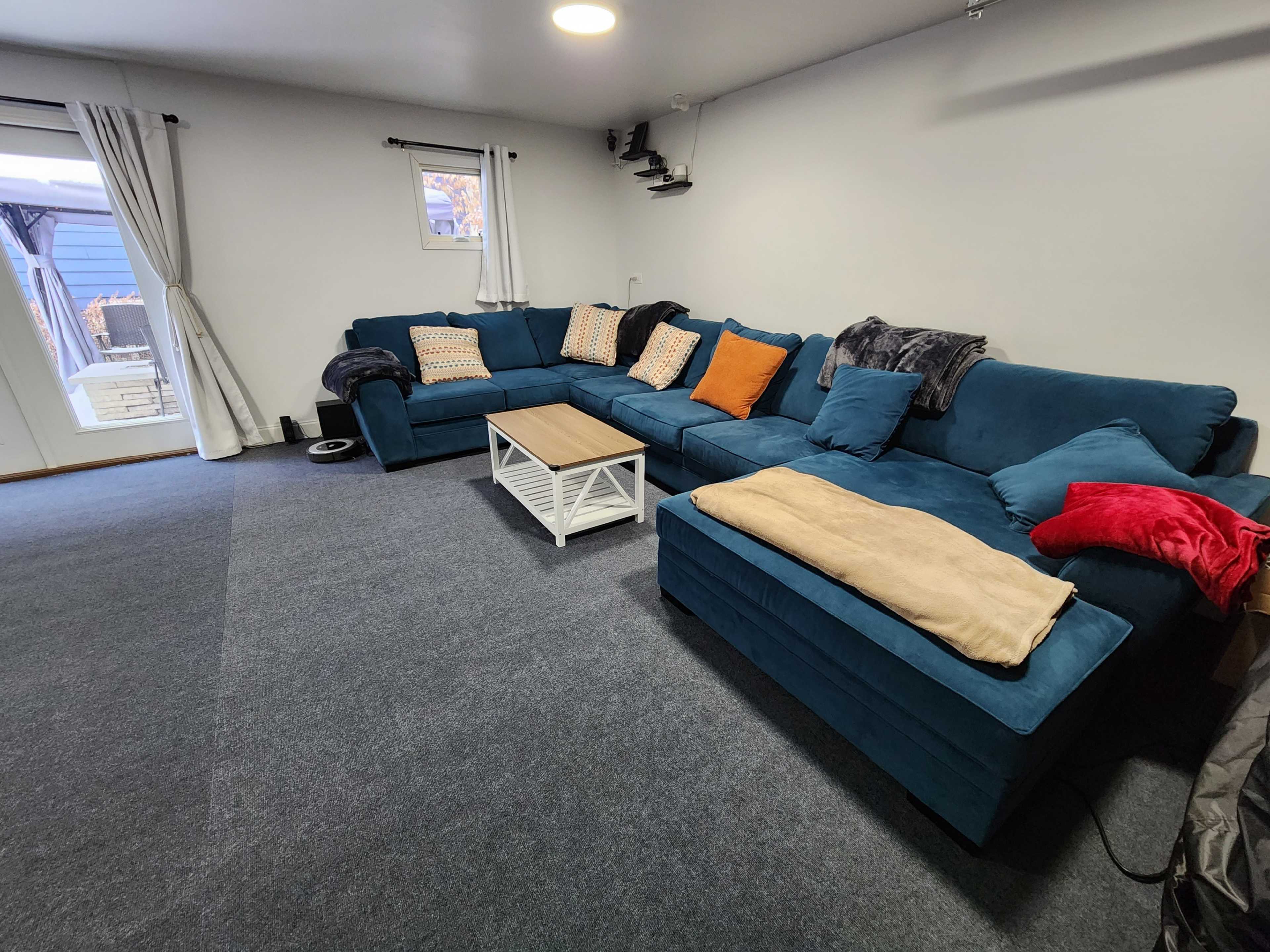 A spacious living area with a blue sectional sofa, a coffee table, and large windows with light-colored curtains.