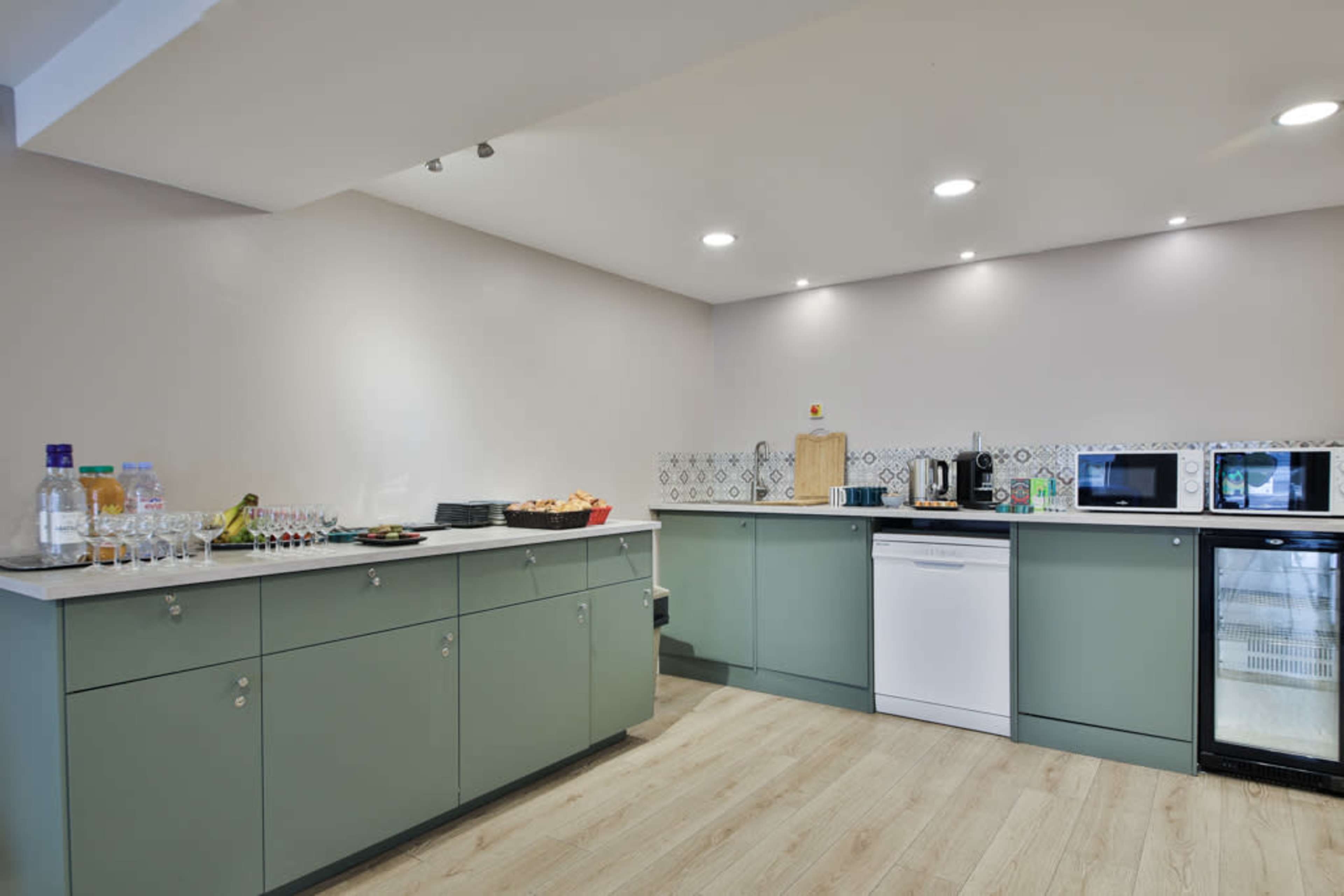 A modern kitchen with green cabinets, a countertop, appliances, and a variety of drinks on the counter.