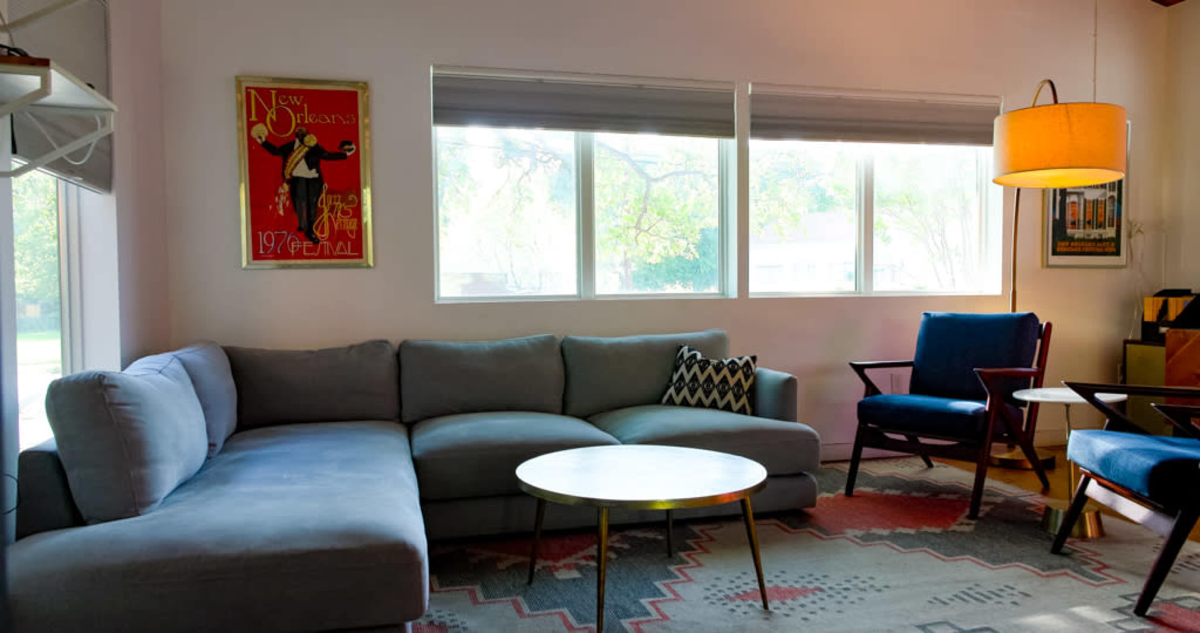 The image depicts a modern living room featuring a sectional sofa, a round coffee table, and large windows with natural light streaming in.