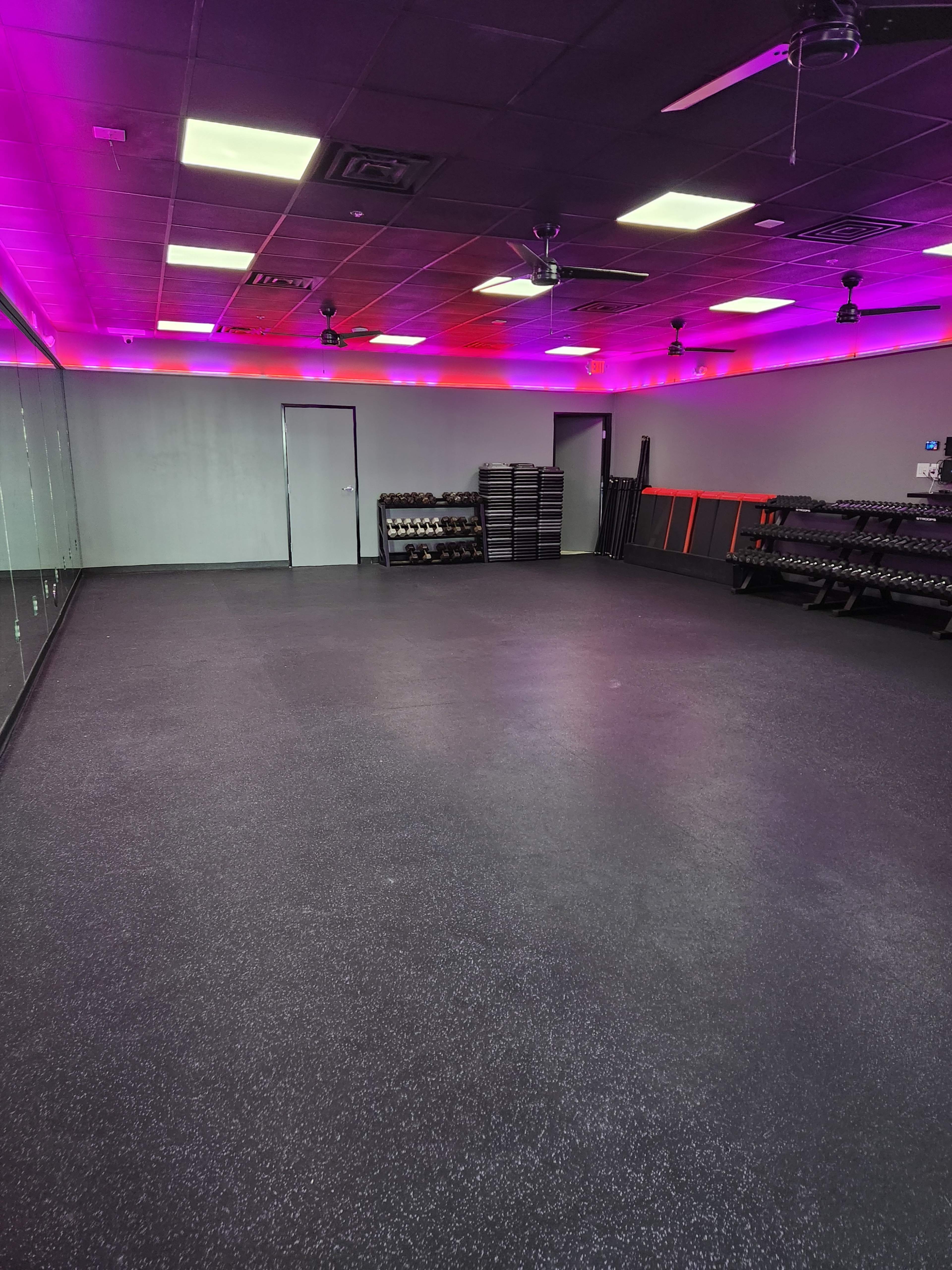A spacious gym room with rubber flooring, mirrored walls, and a row of weights along one side.