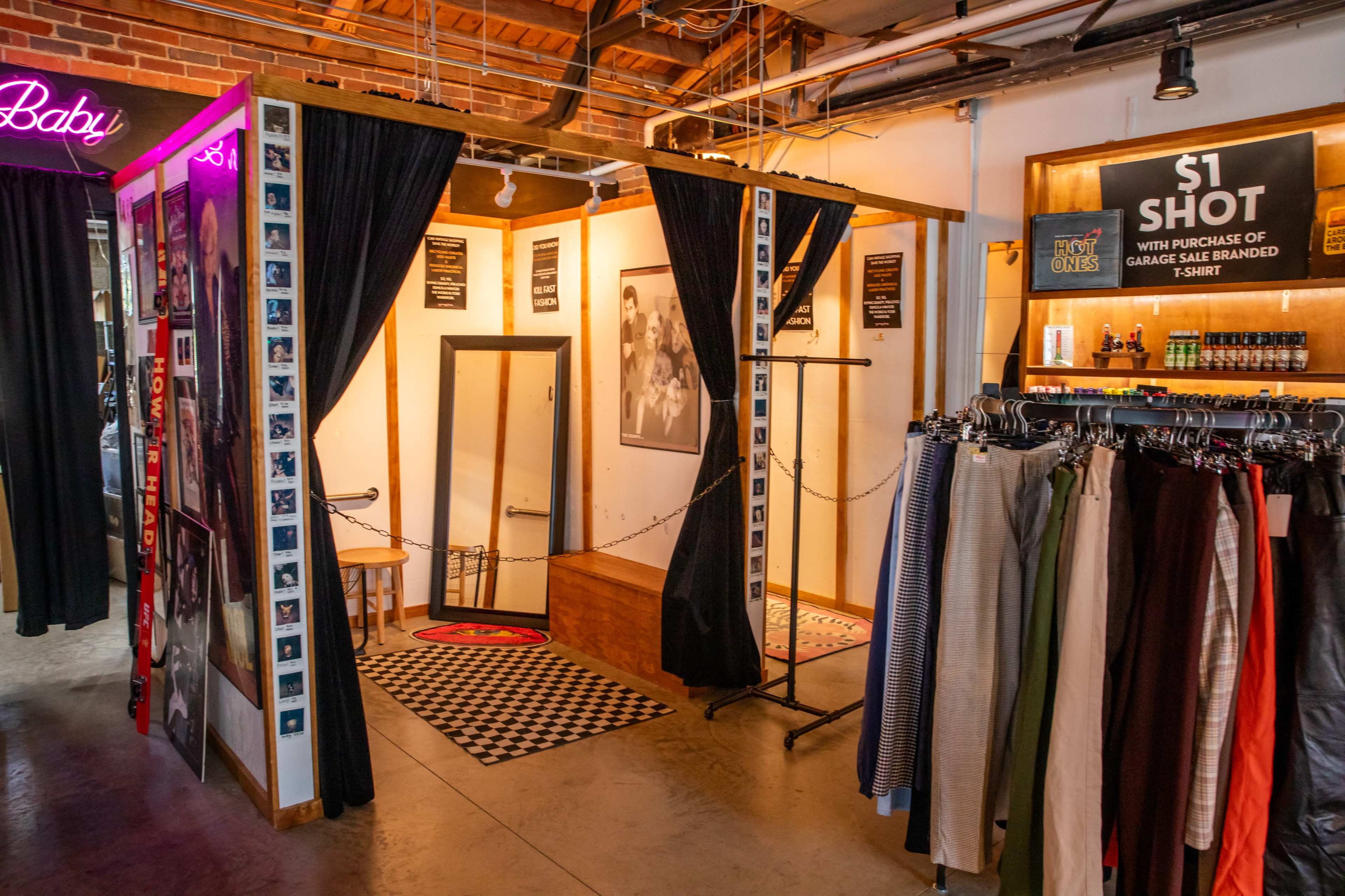 The image shows an indoor space featuring a photo booth area with a checkered rug and draped curtains, adjacent to a retail section displaying various pants and a bar with beverages.