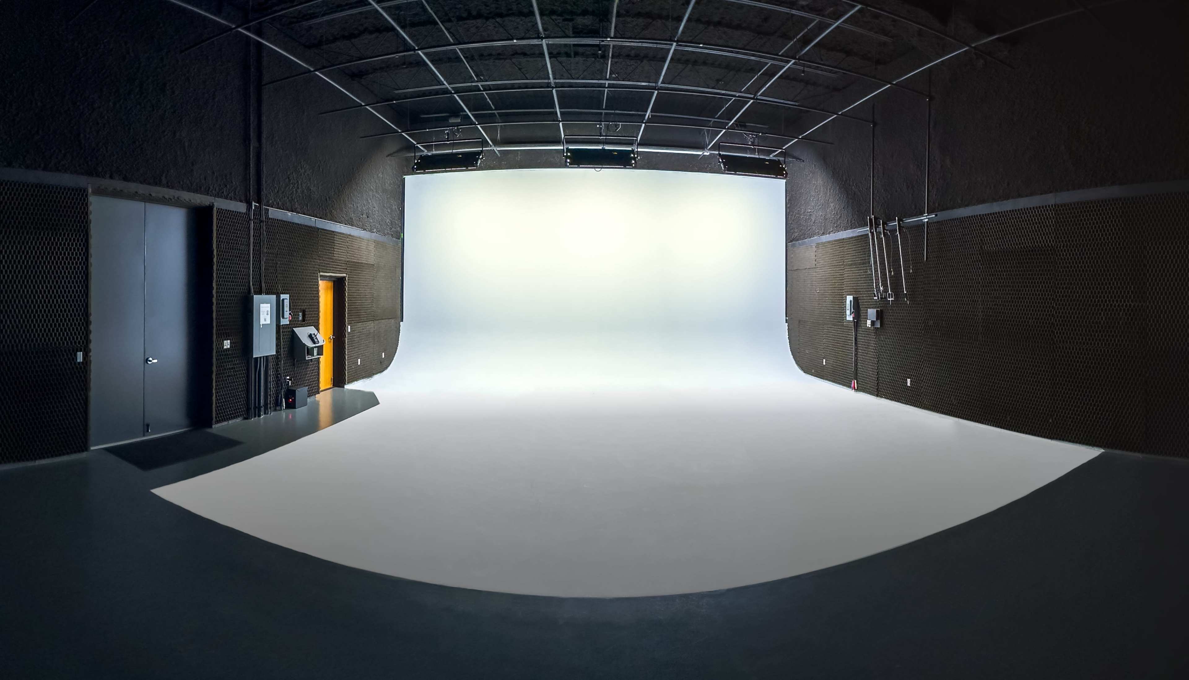 The image shows a spacious photography studio with a seamless white backdrop and gray walls.