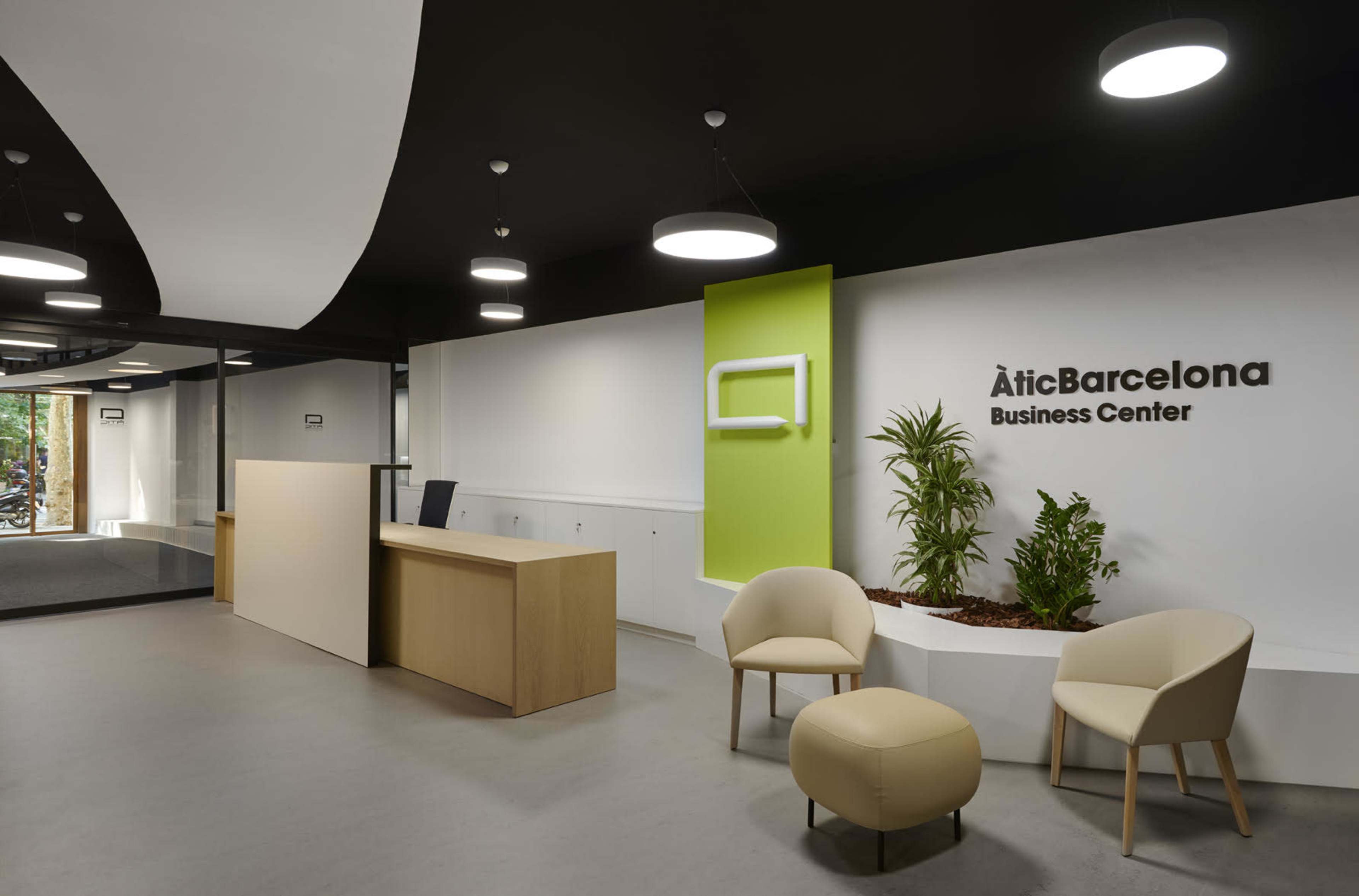 The image shows a modern reception area of a business center featuring a front desk, seating arrangements, and indoor plants.