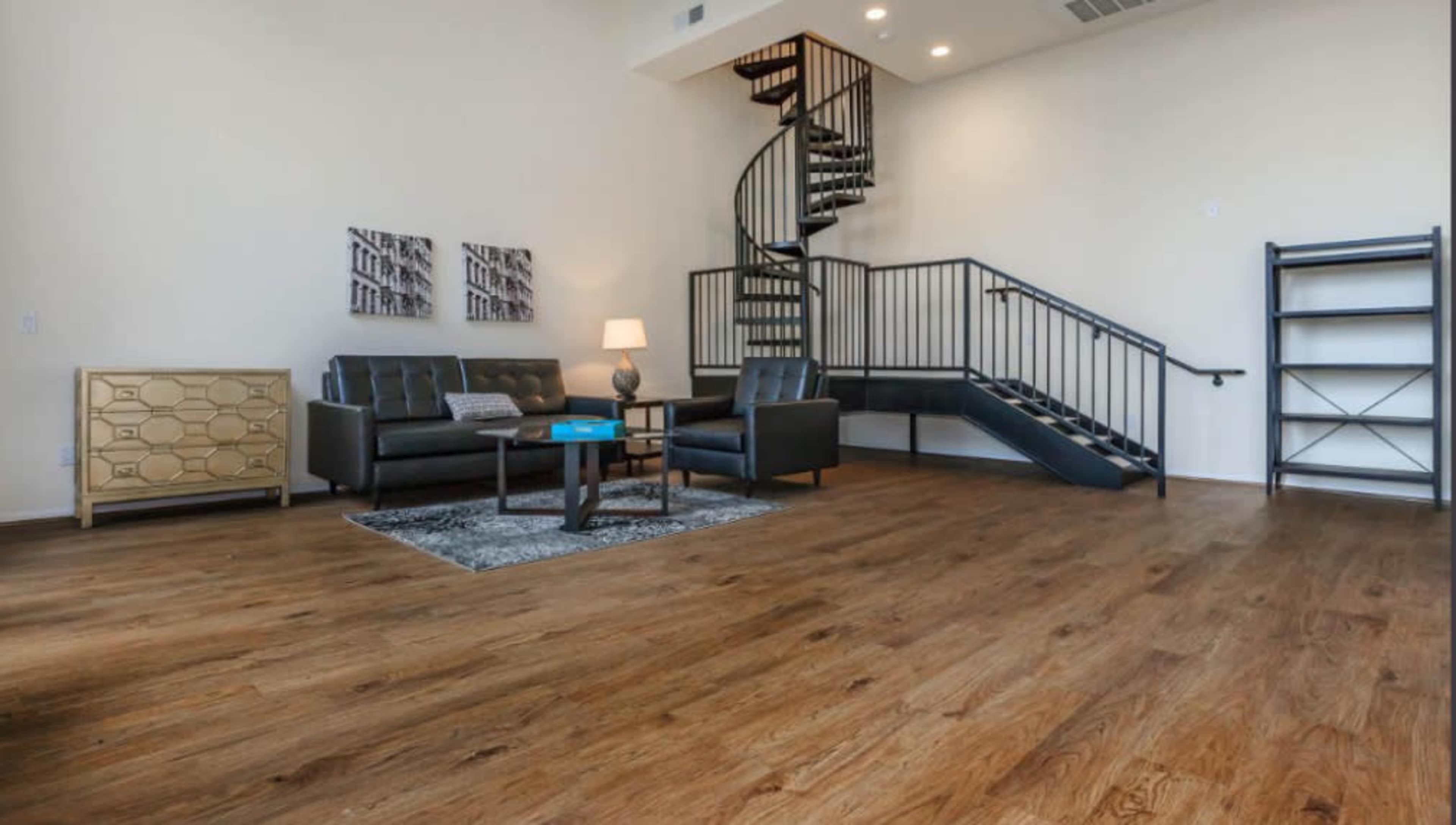 The image shows a modern living room featuring a spiral staircase, hardwood flooring, a sofa set, a coffee table, and a bookshelf.