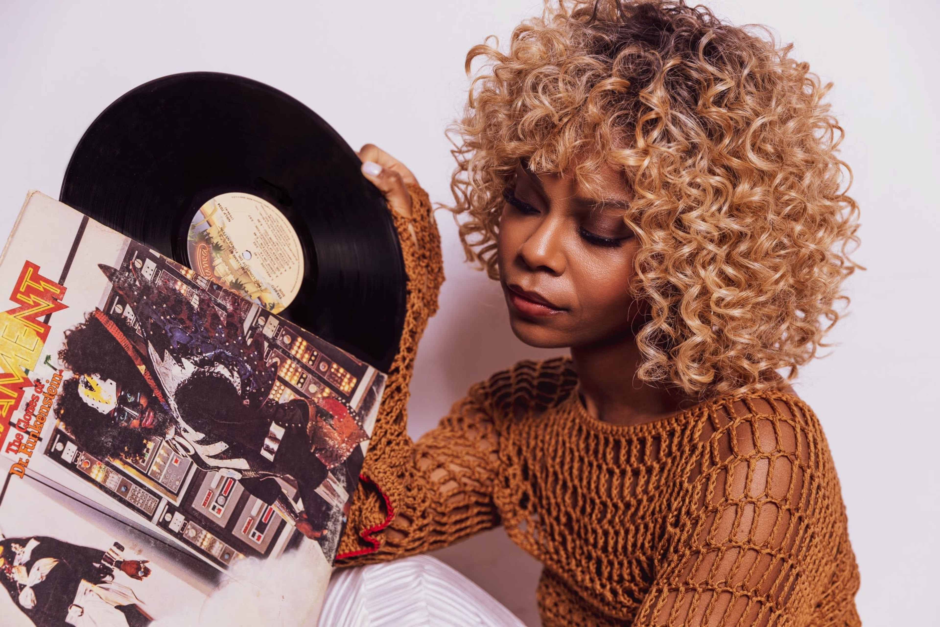 A person with curly hair holds a vinyl record and looks thoughtfully at its cover.