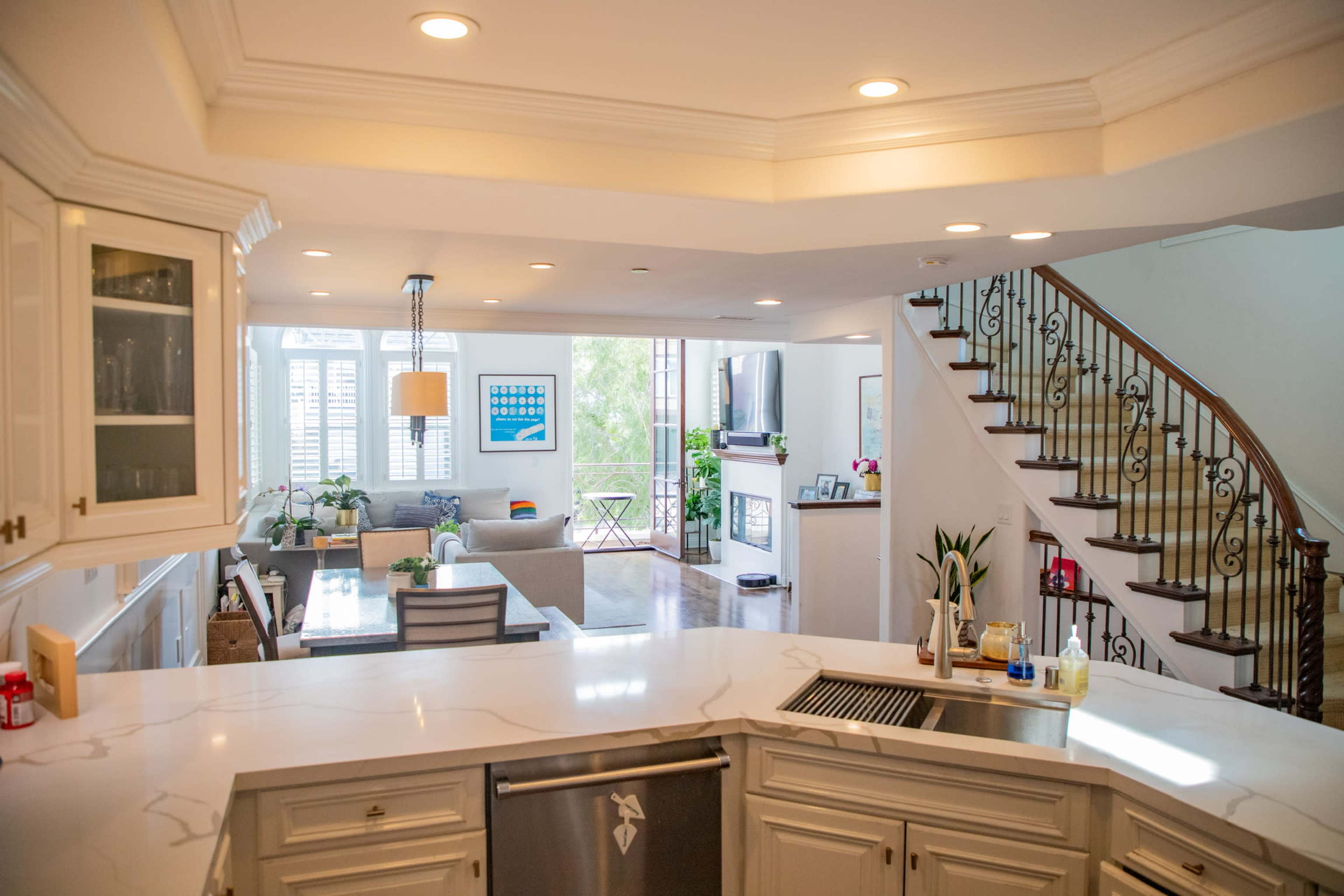 The image shows a modern open-concept kitchen with a marble countertop that overlooks a living area and a staircase.