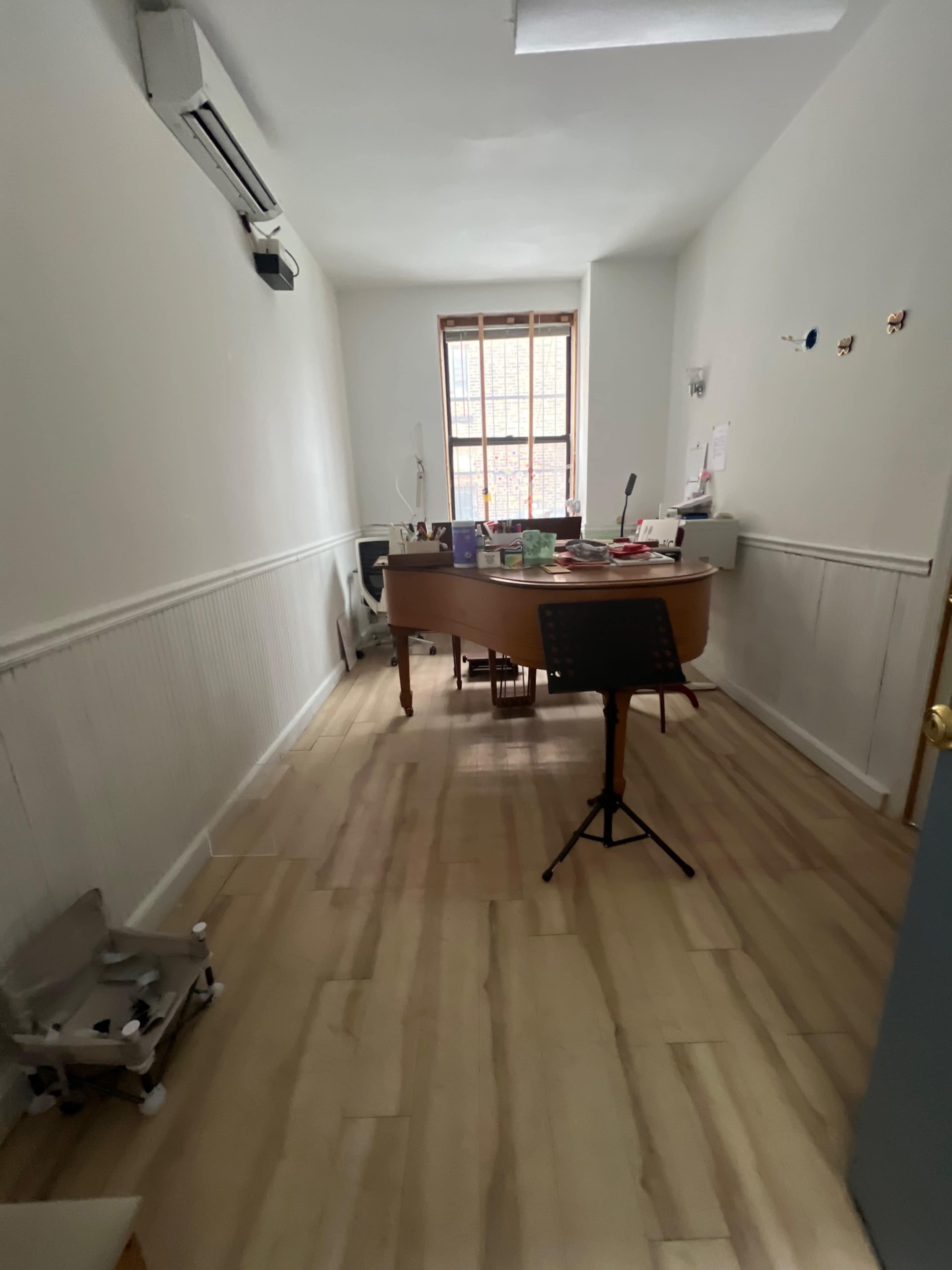 The image shows an empty office space with light-colored wooden flooring, a circular desk in the center, and minimal furniture along the walls.