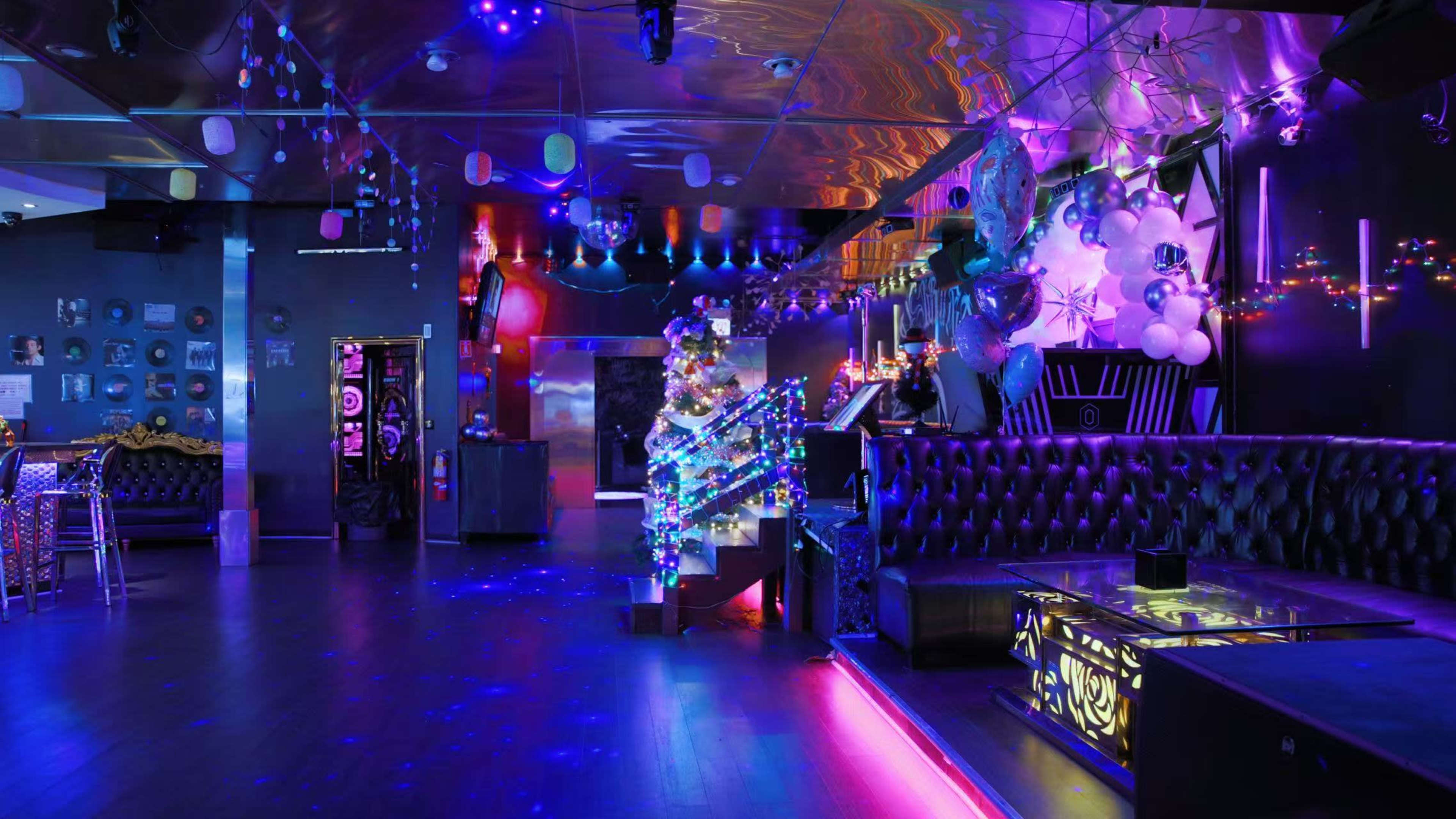 The image shows a vibrant nightclub interior illuminated by colorful lights, with a bar area and stylish seating arrangements.