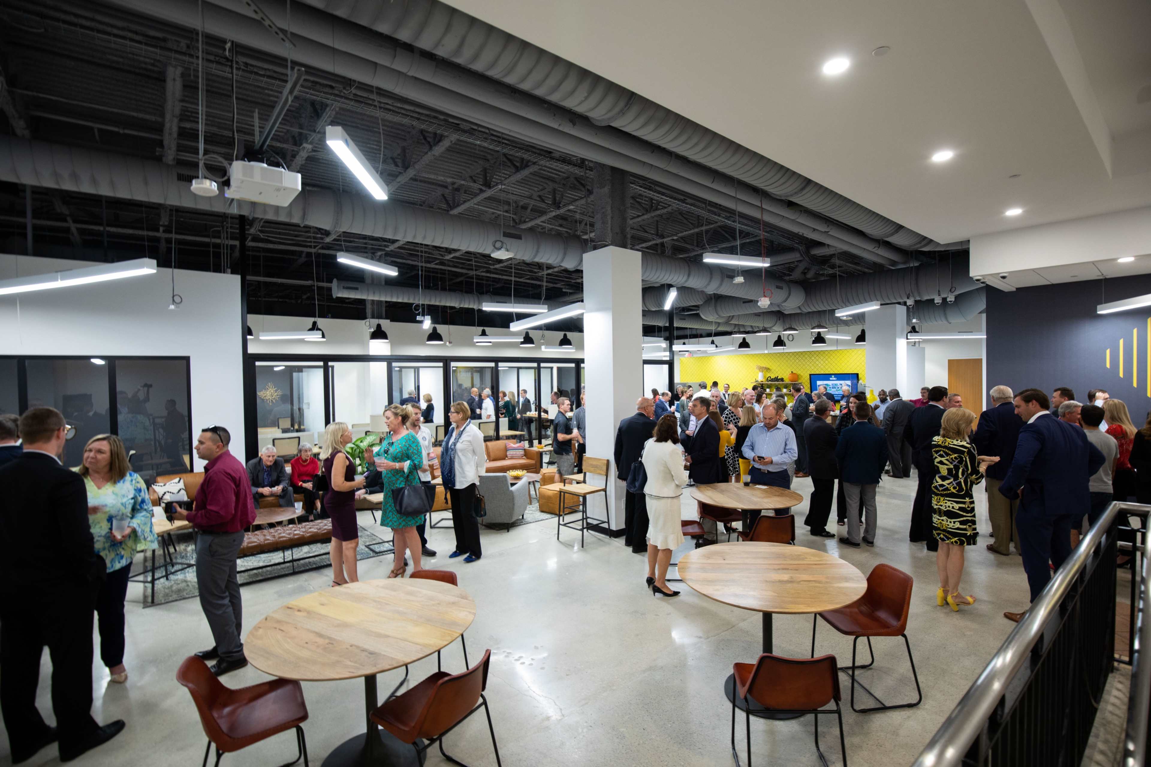 A large group of people is mingling in a modern office space with tables and couches.