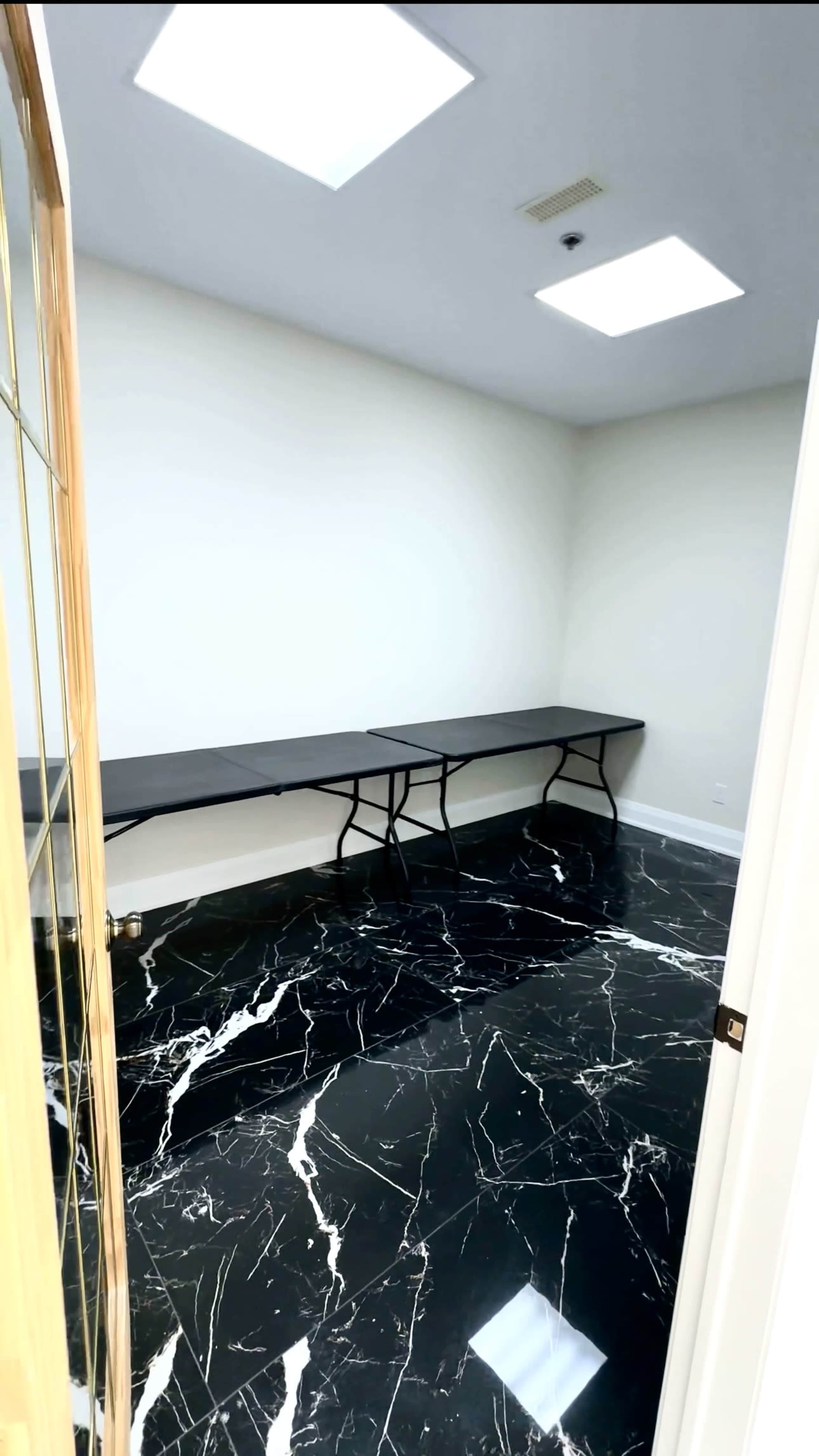 The image shows a small room with black marble flooring, featuring two folding tables along one wall and a door partially open.