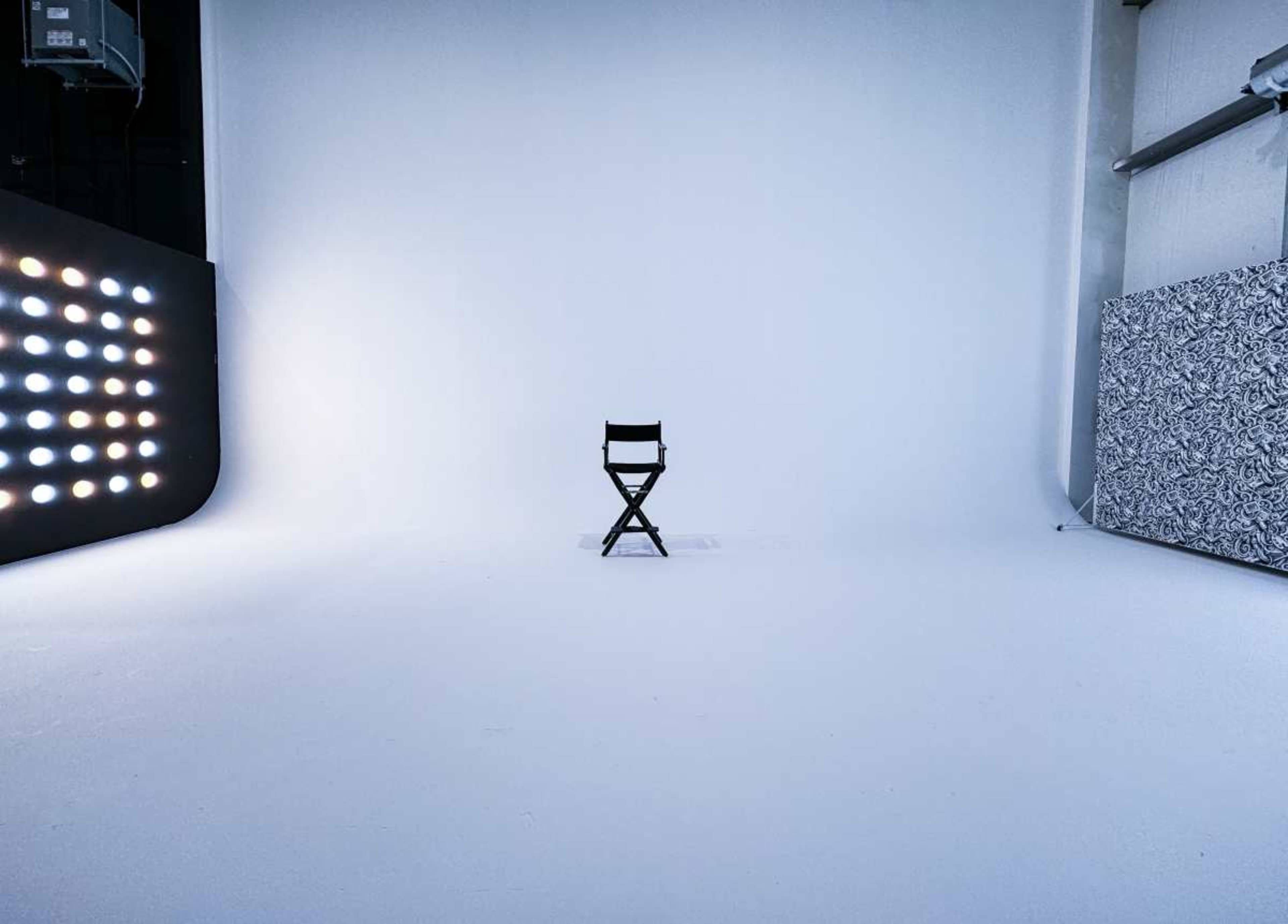 A single black director's chair stands on a plain white studio backdrop surrounded by soft lighting.