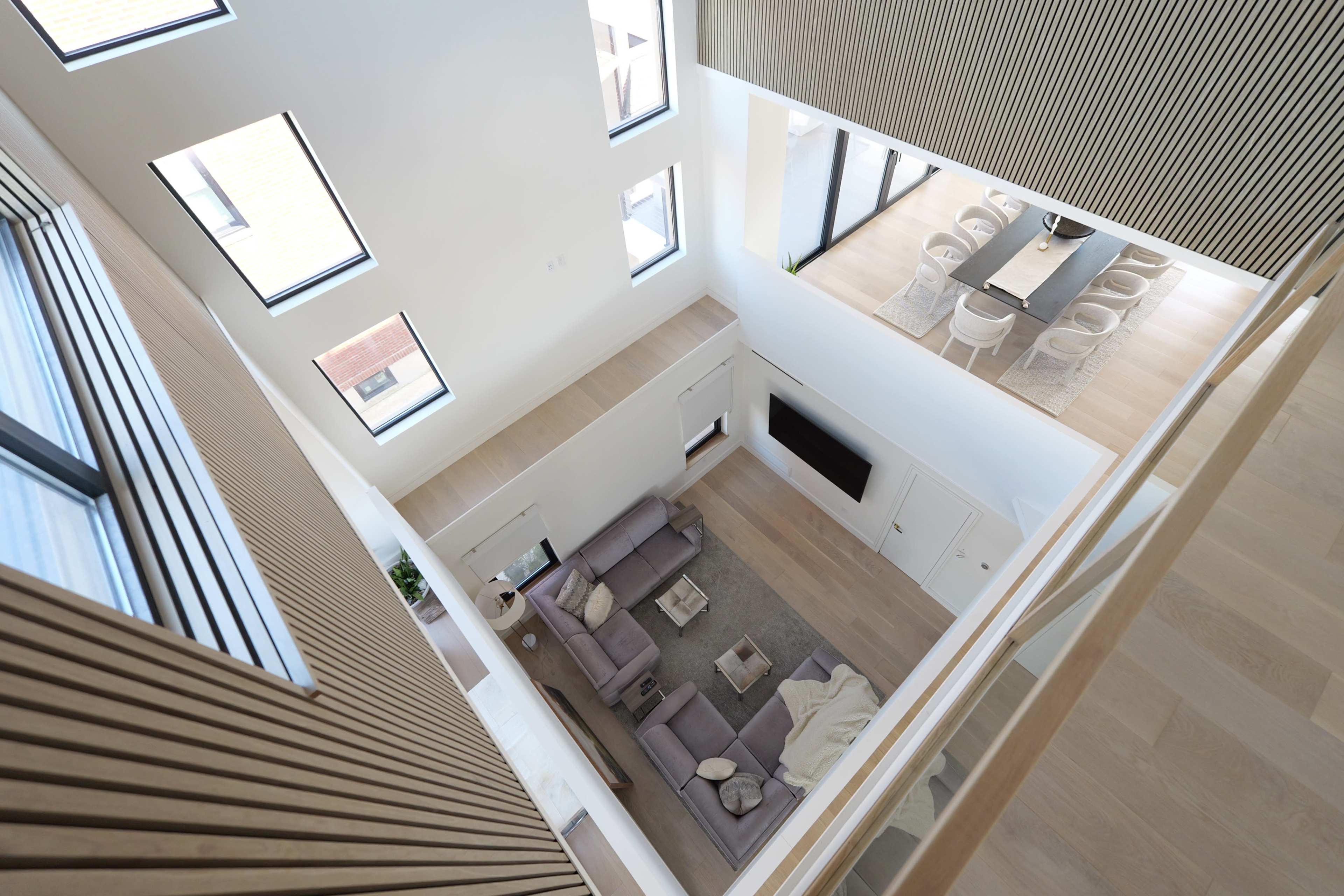The image shows an interior view of a modern two-story living space with a sectional sofa, a coffee table, and a dining area visible above.