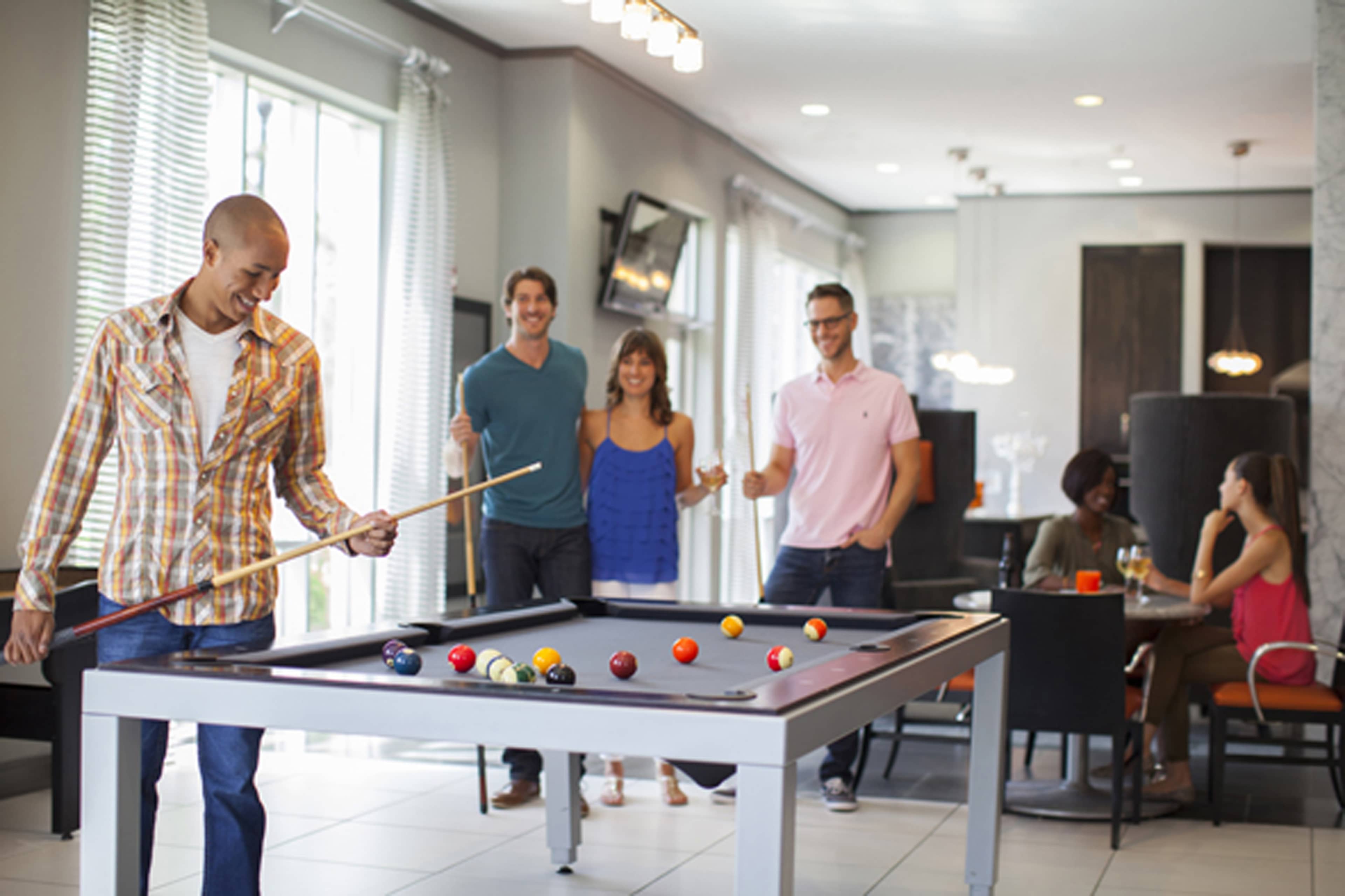 A group of four people socialize in a recreational area while one person prepares to take a shot at a pool table.