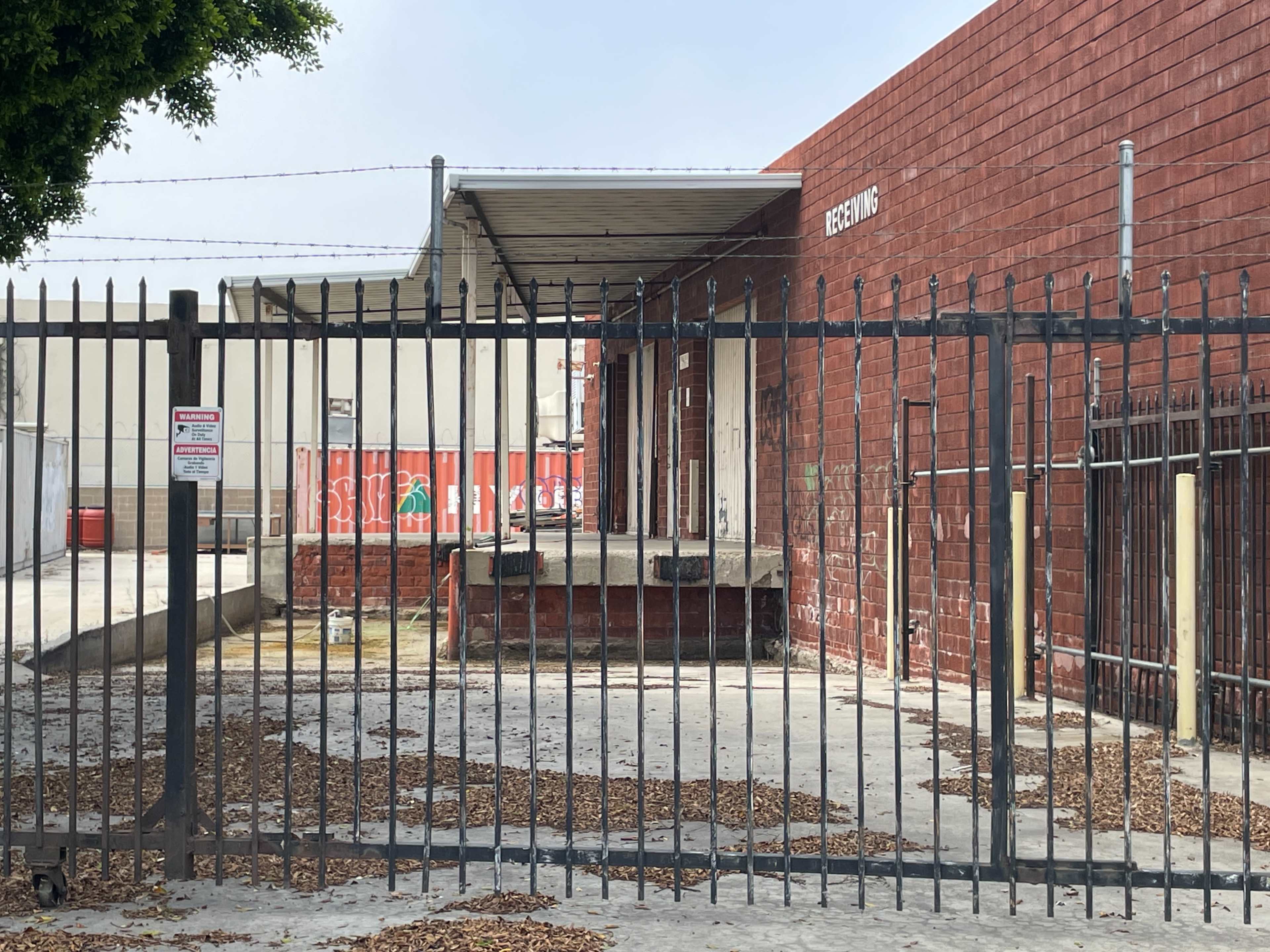 A gated industrial area with a brick building and a loading dock is visible, with scattered leaves on the ground.