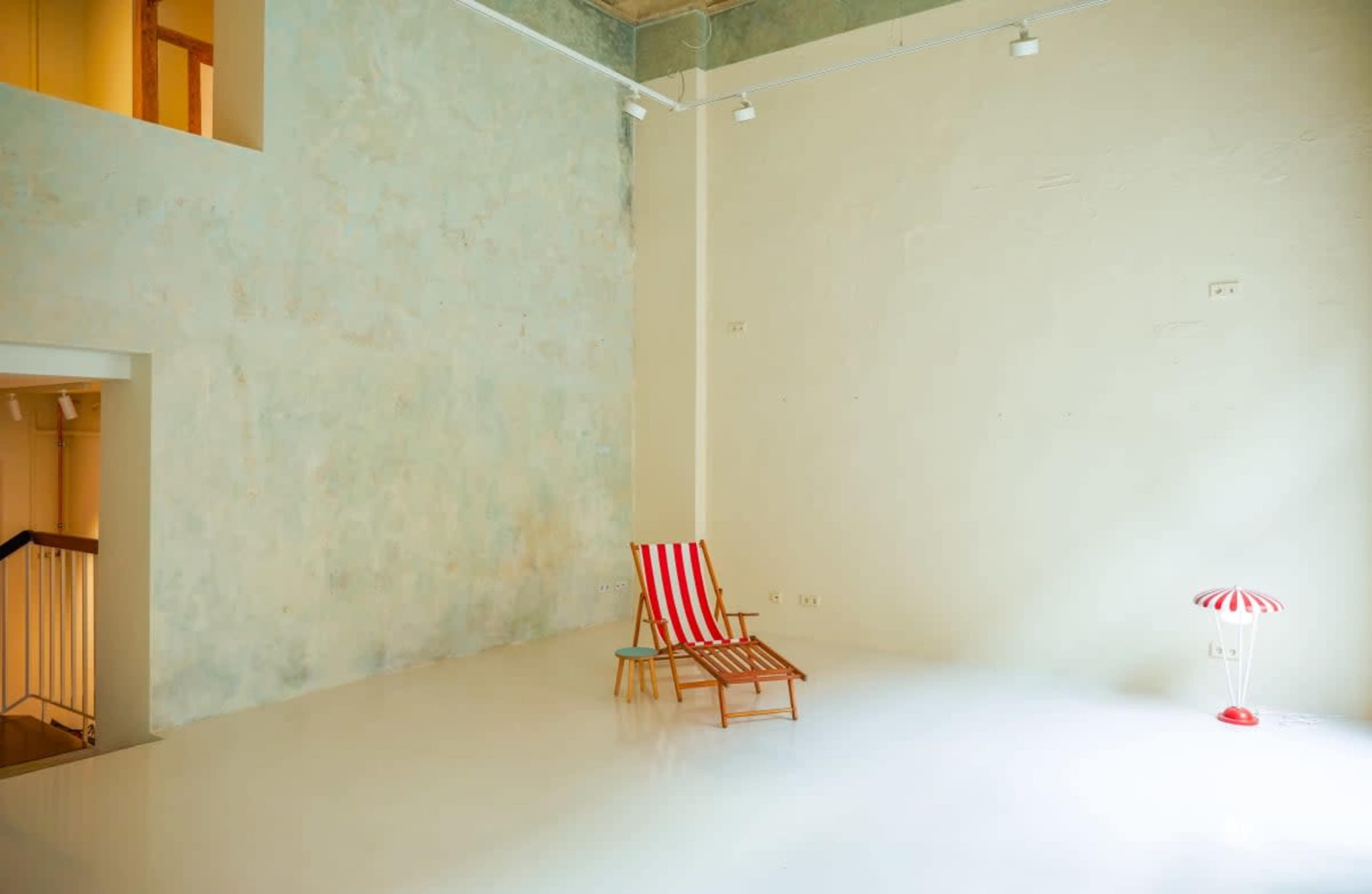 The image shows a minimalist room with a striped lounge chair and a small table, featuring a white floor and a textured wall.