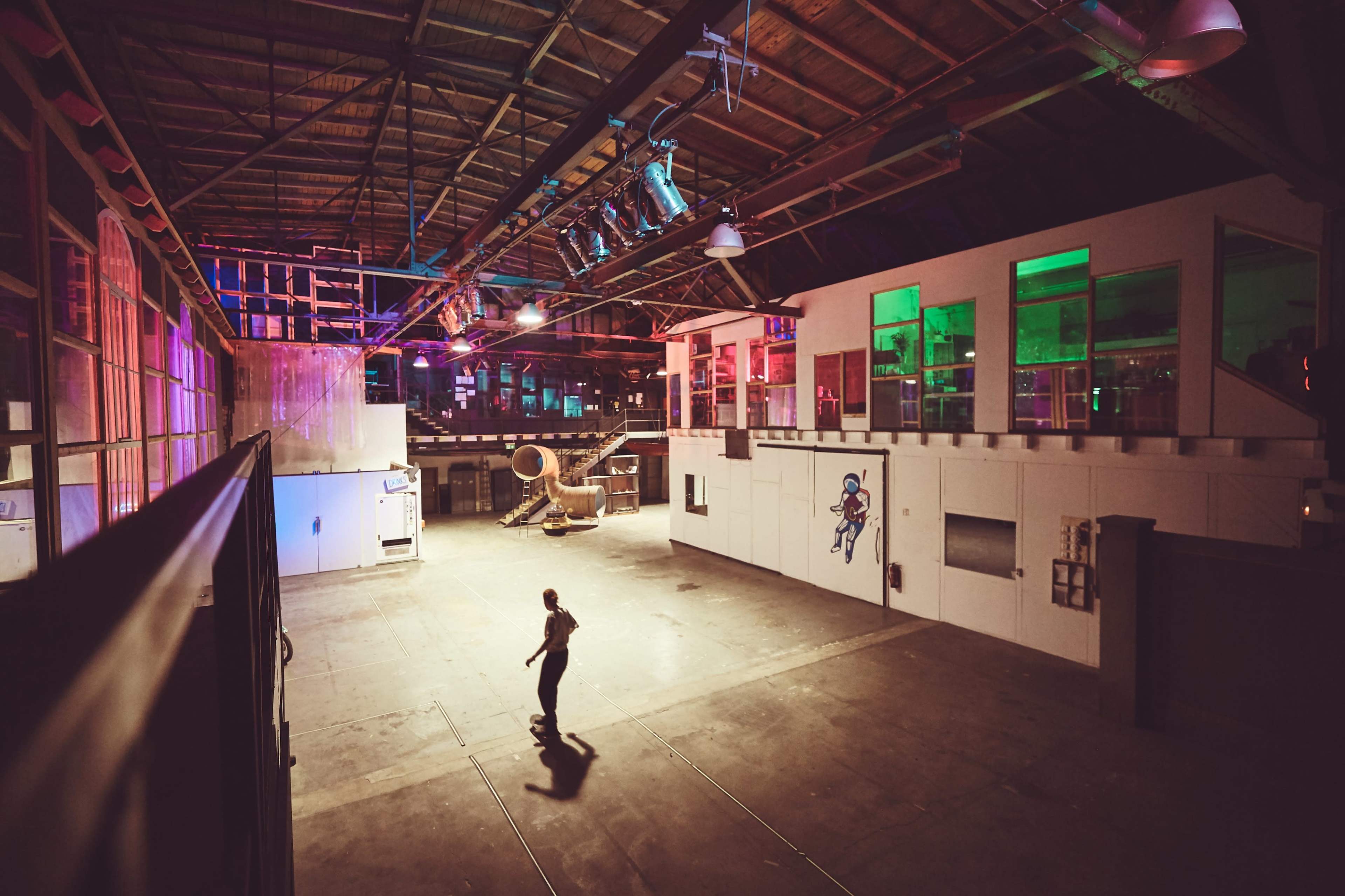 An empty warehouse features colorful lights, large windows, and a person walking across the concrete floor.