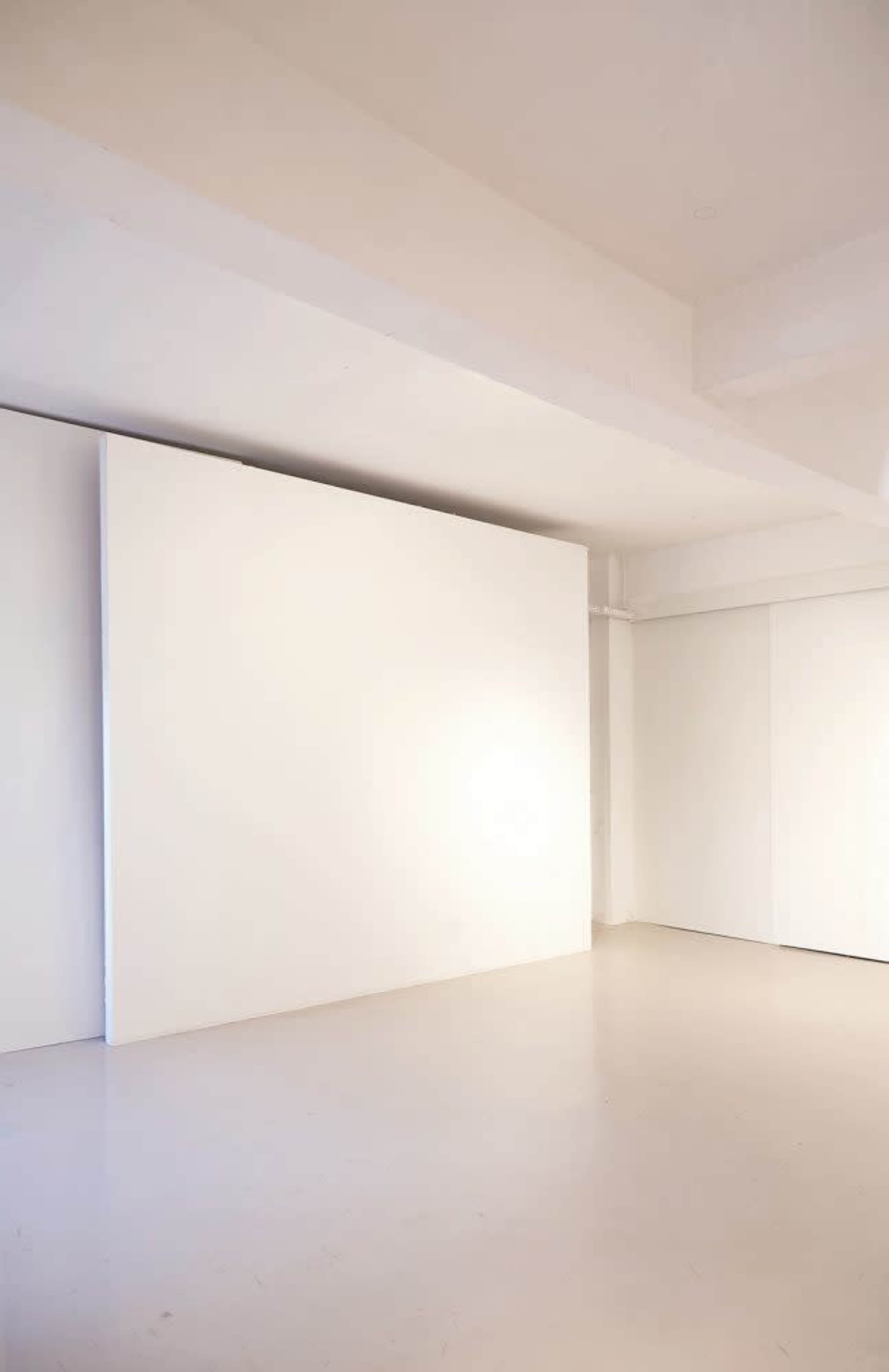 The image shows a minimalist interior space with white walls and a light-colored floor.