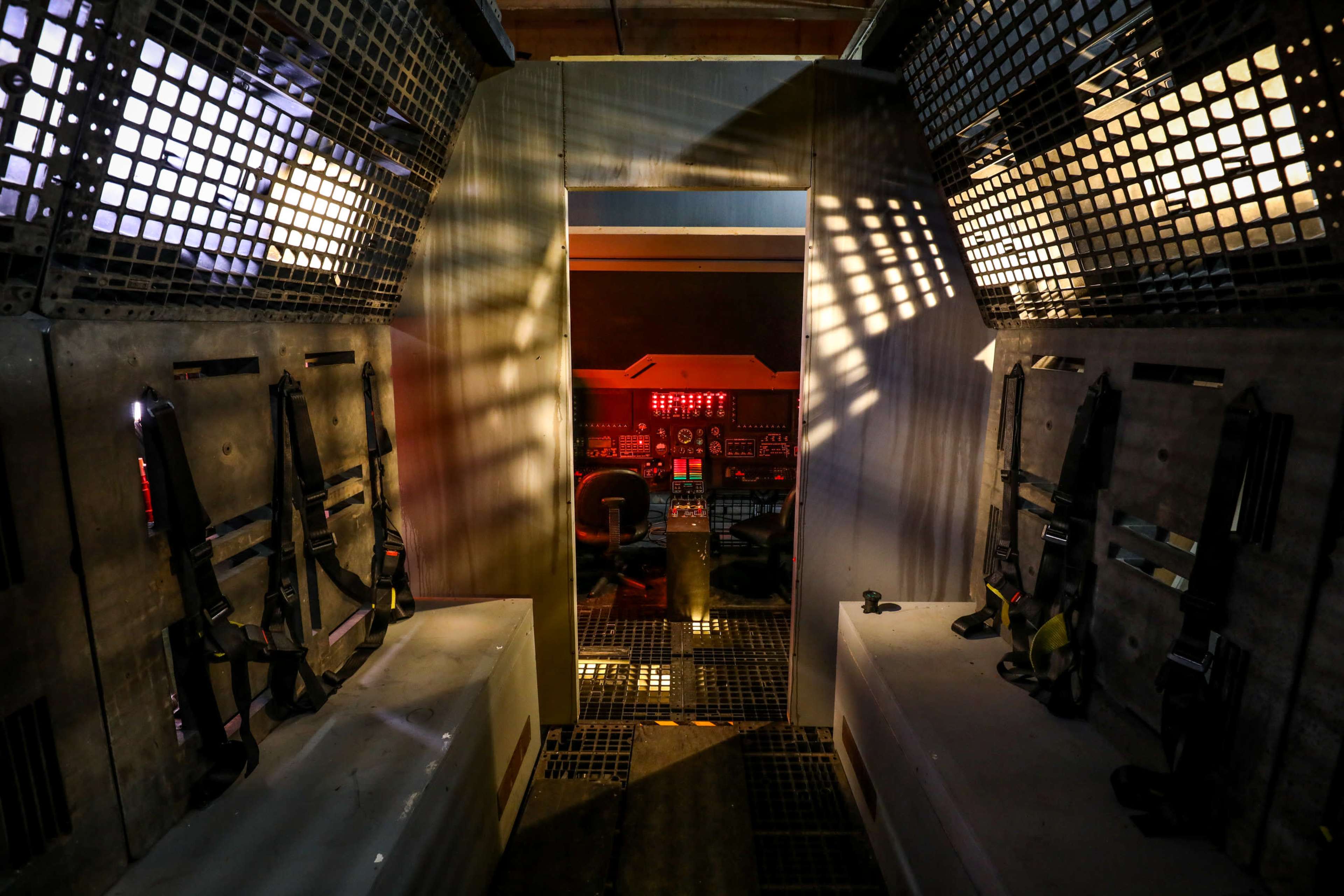 The image shows a dimly lit corridor leading to a control room, with weapons mounted on the walls and red lighting illuminating the space.