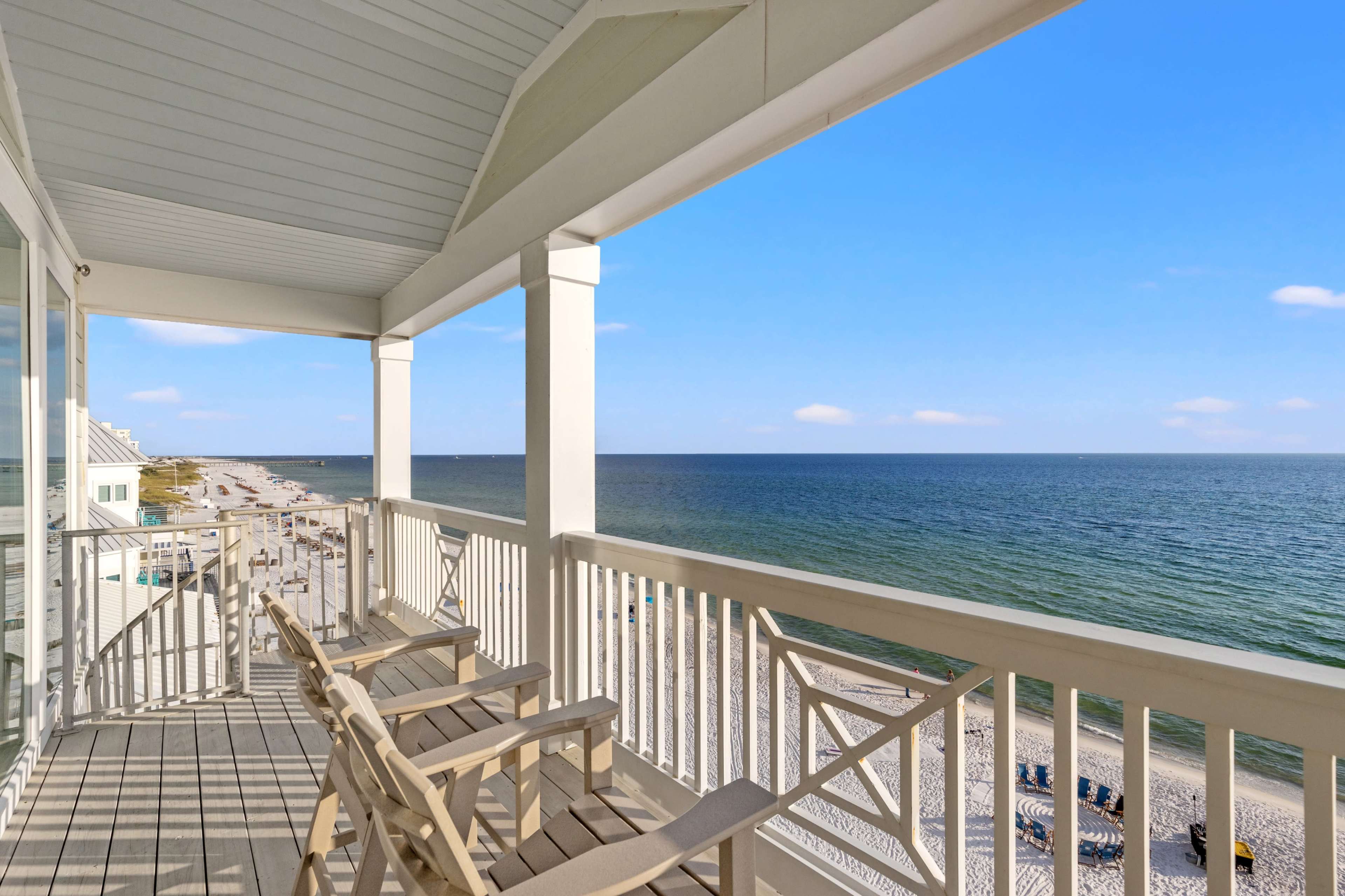 The image shows a beachfront balcony overlooking the ocean, with wooden chairs positioned for viewing the sea and shoreline.