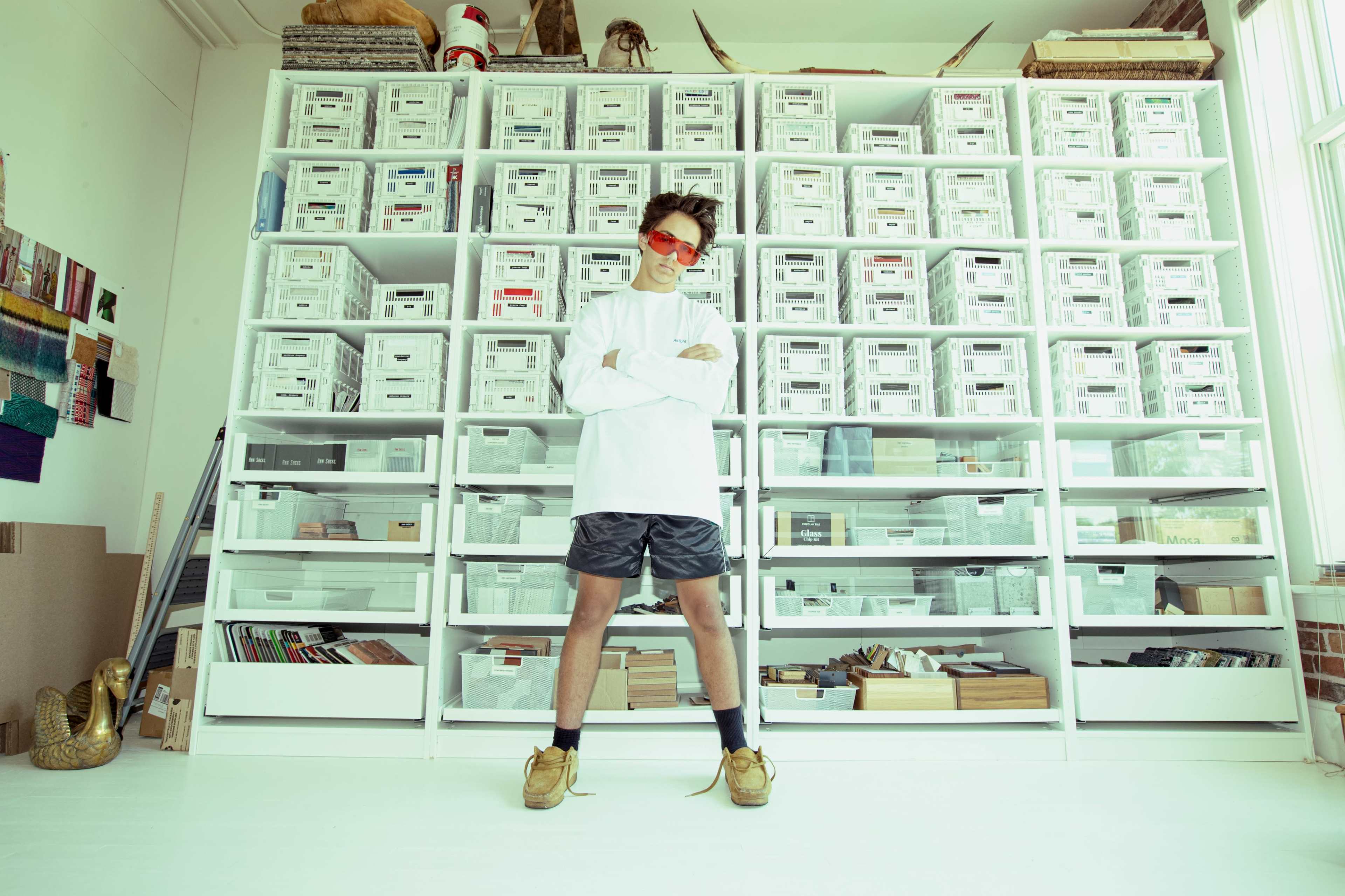 A person stands confidently in front of a large shelving unit filled with labeled storage boxes.