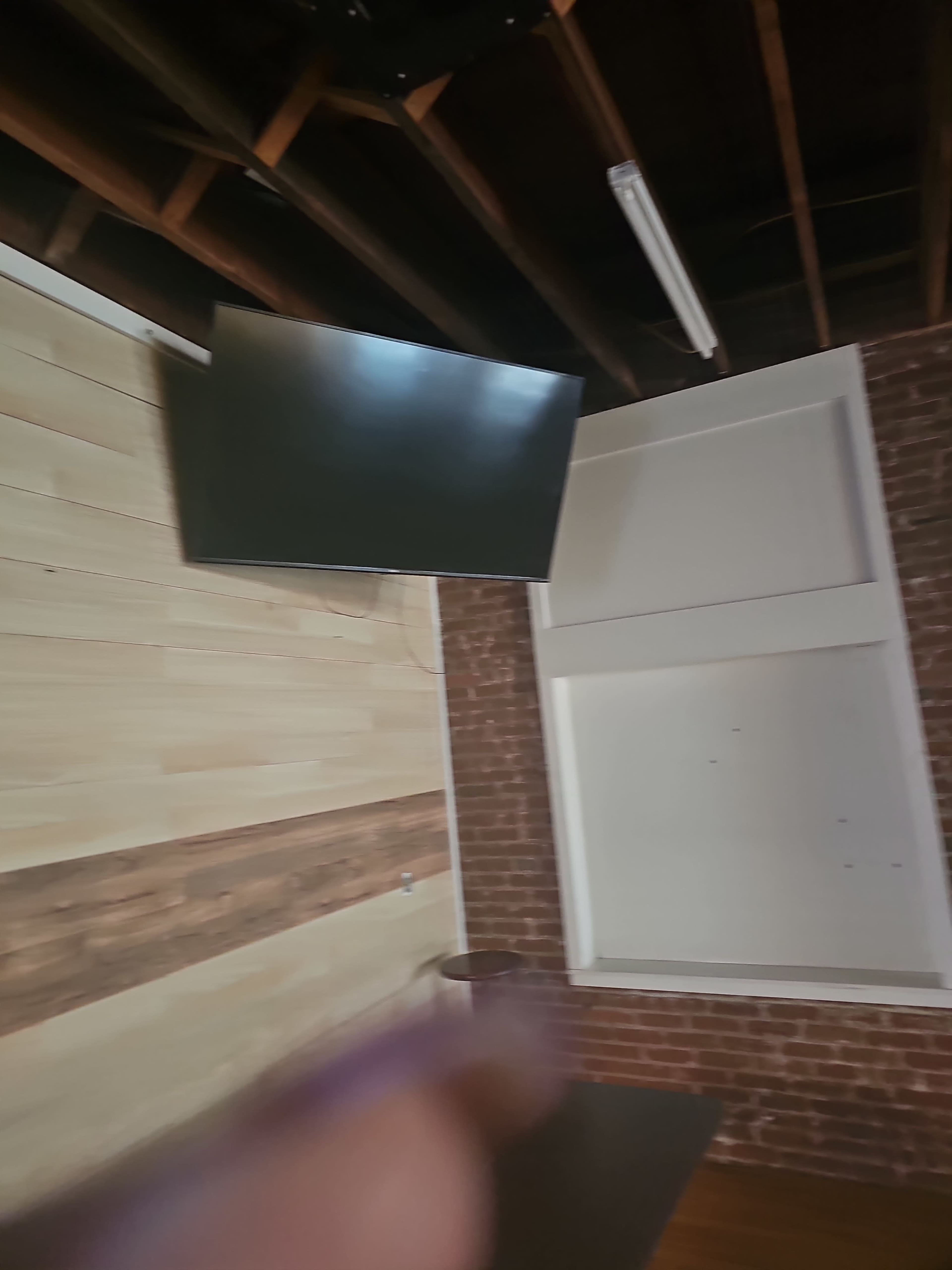 A wall with exposed wooden beams and a mounted TV, adjacent to a brick wall with a white panel.