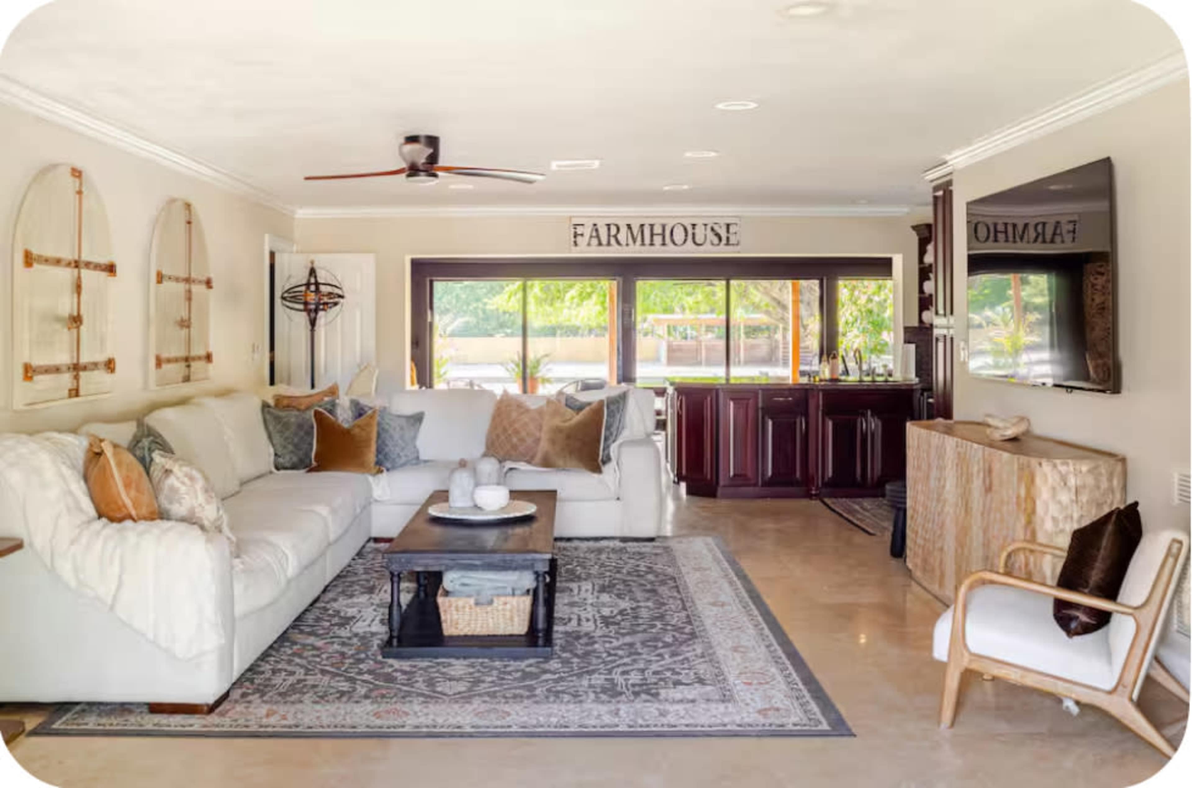 The living room features a large sectional sofa with decorative pillows, a wooden coffee table on a patterned rug, and a view of a kitchen area with dark cabinetry.