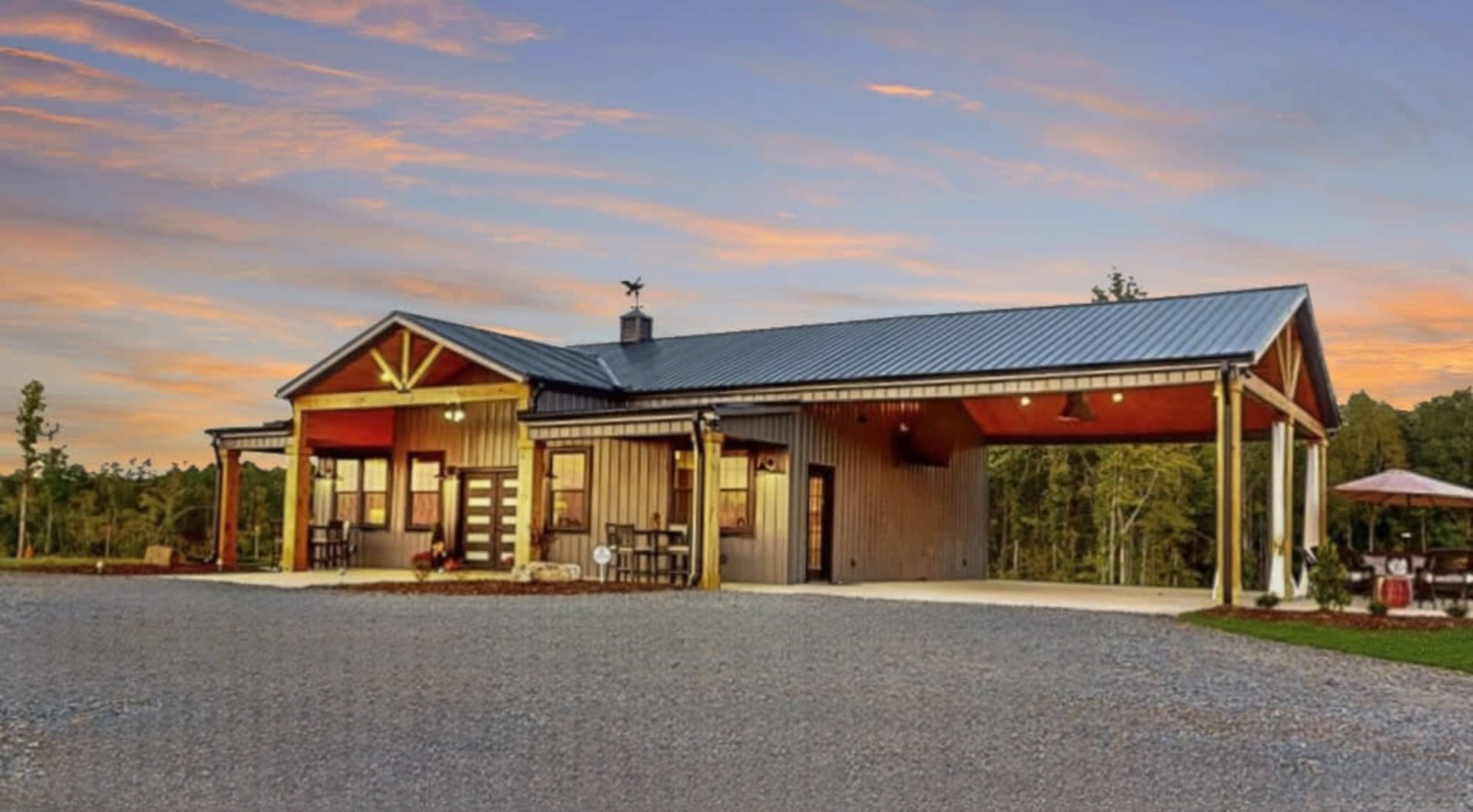A modern single-story building with a metal roof and wooden accents, set against a colorful sunset sky.
