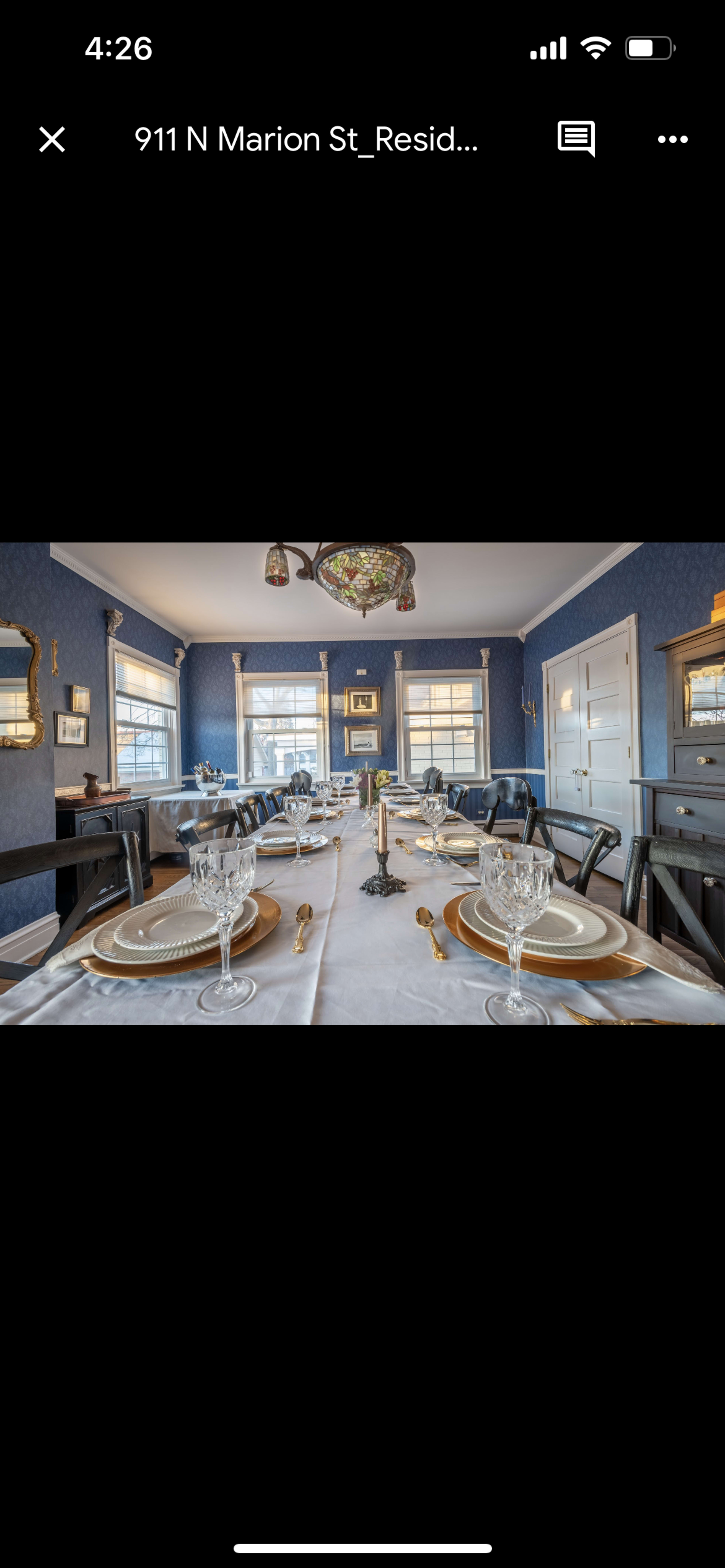 A dining room set for a formal meal, featuring a long table with elegant place settings, crystal glassware, and blue wallpaper.