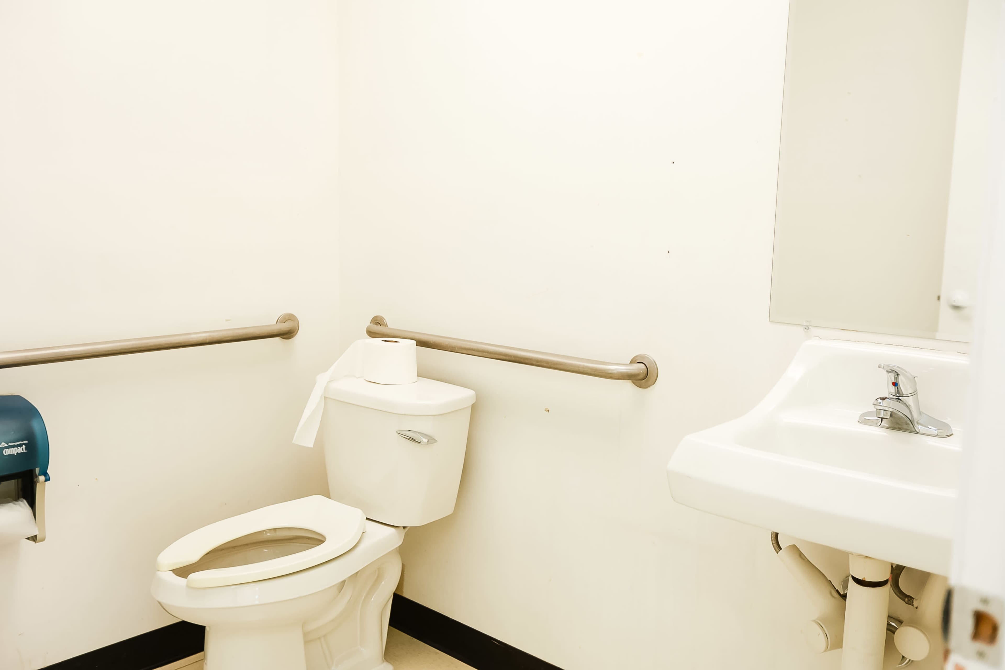 A restroom with a toilet, a sink, and grab bars on the walls.