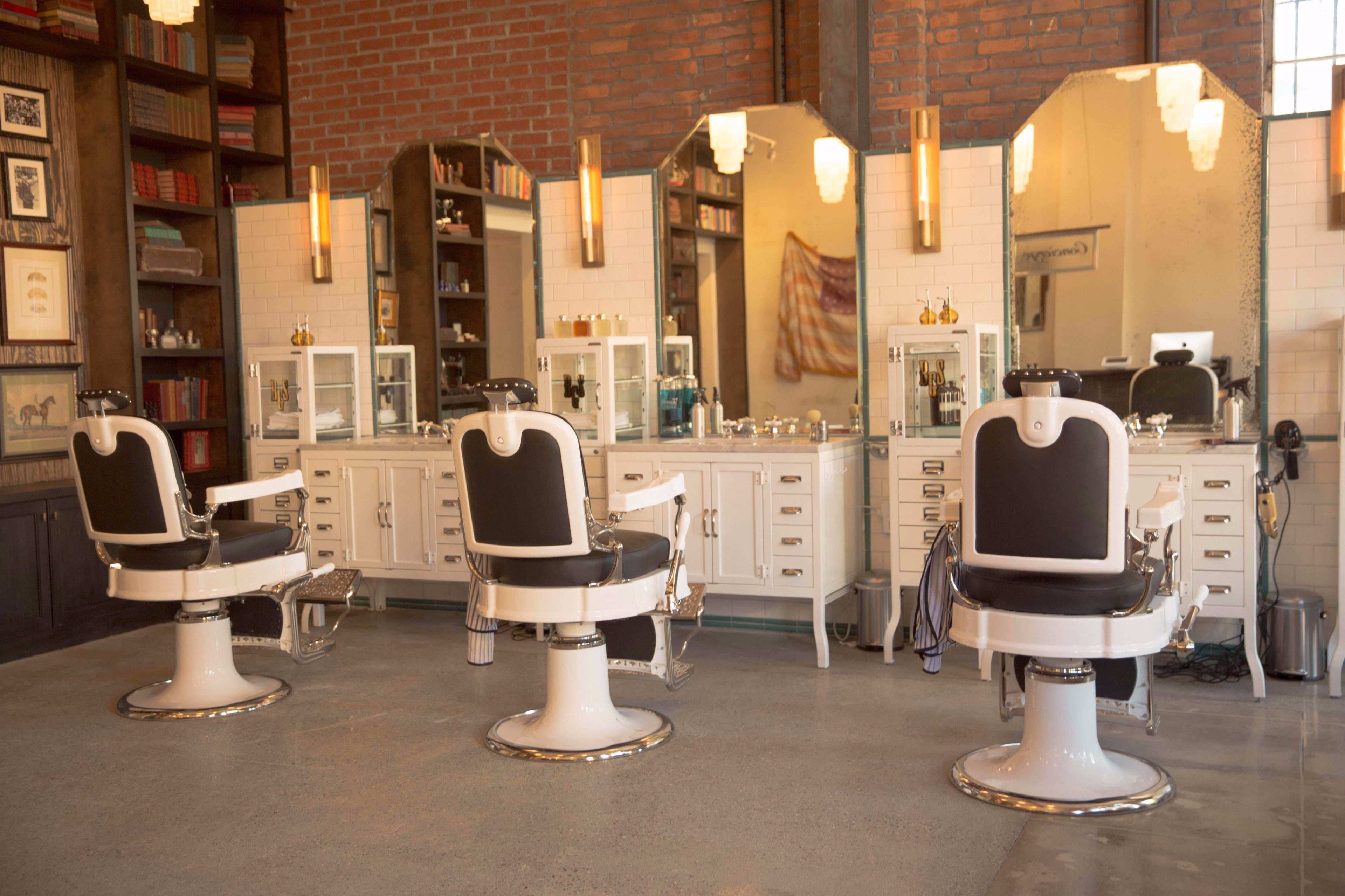 The image shows a vintage-style barber shop interior with three elegant barber chairs and tall mirrors against a brick wall.