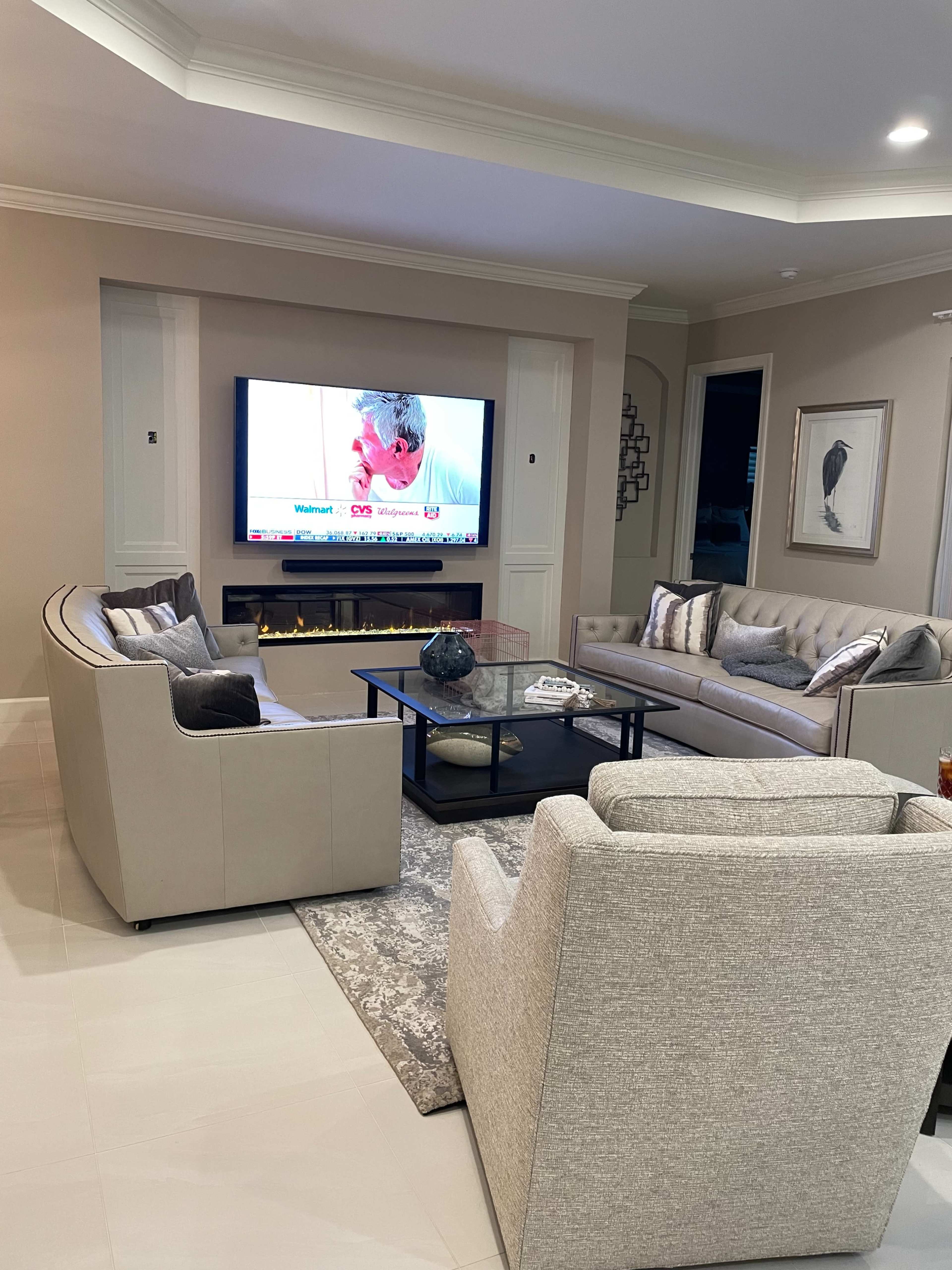 A modern living room with a television mounted on the wall, two light-colored sofas, and a coffee table on a patterned rug.