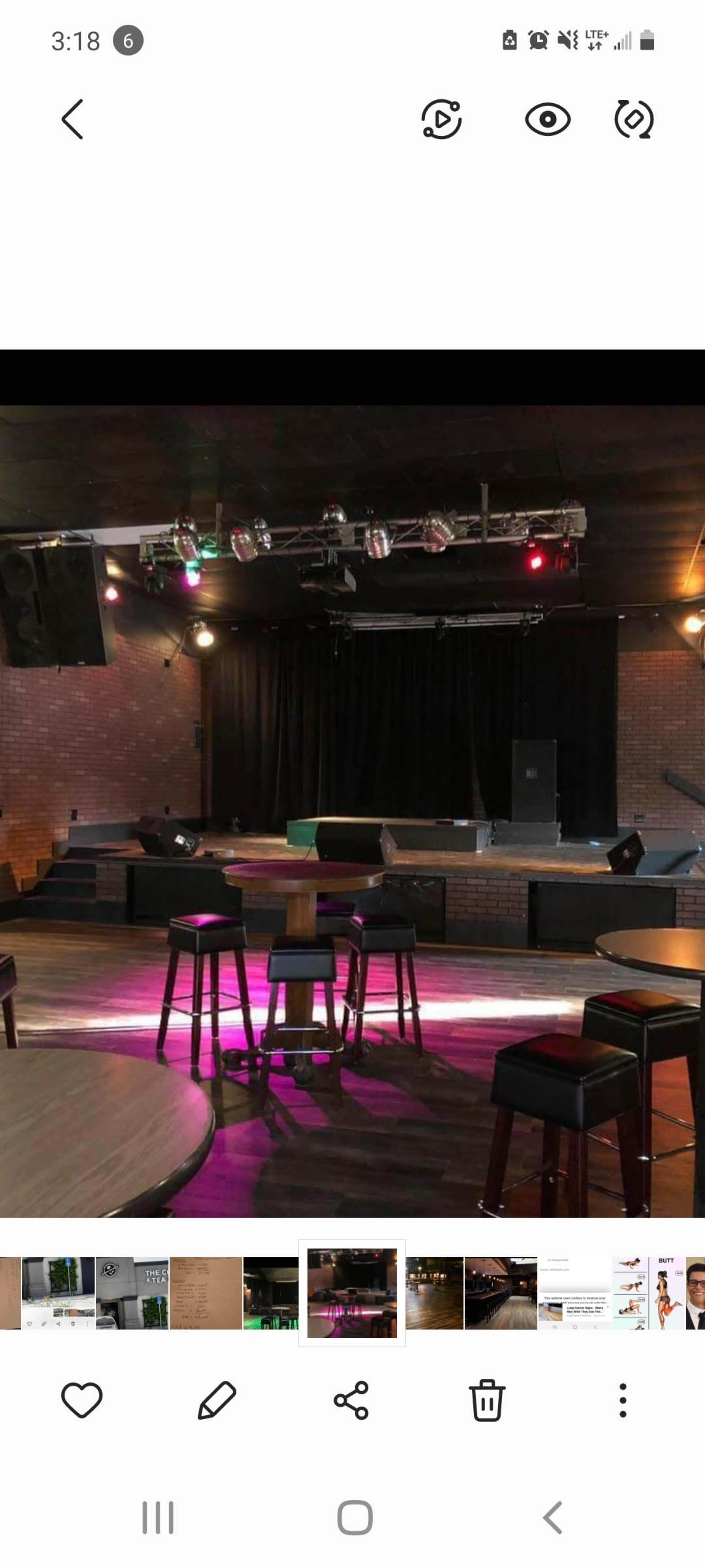 A dimly lit music venue featuring a stage with lights, surrounded by empty tables and stools.