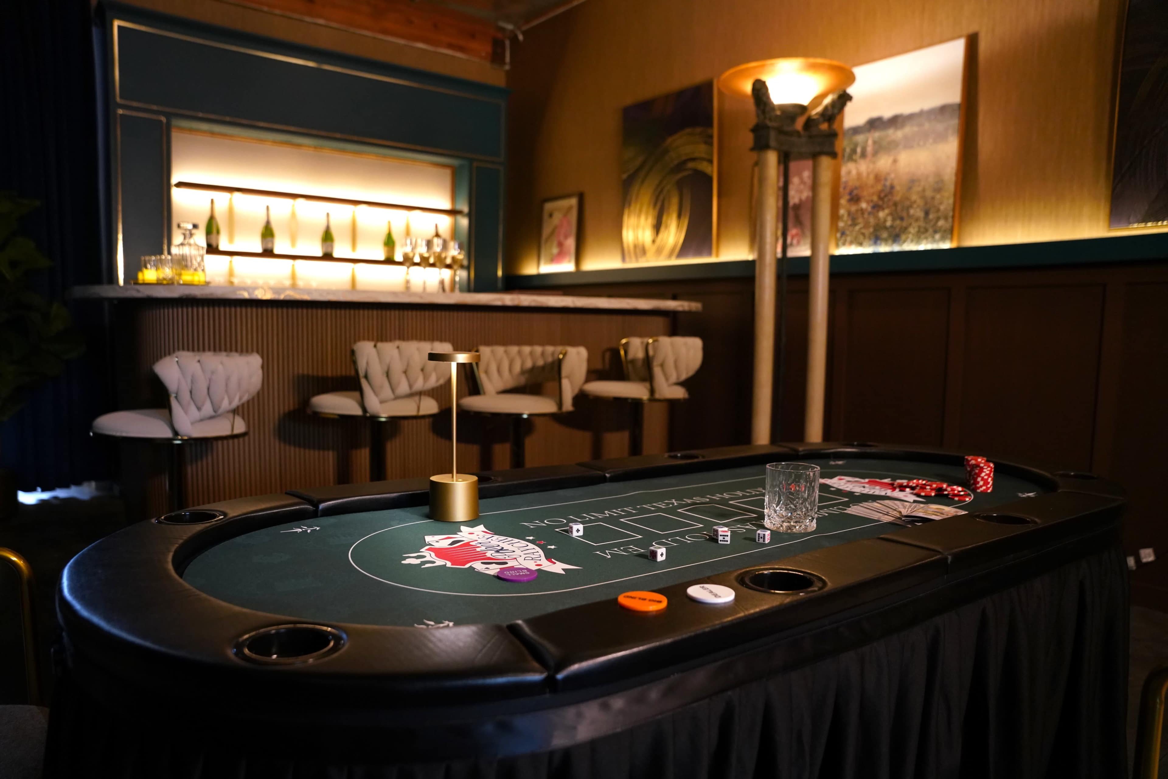 A green felt blackjack table sits in a dimly lit room with a modern bar in the background.